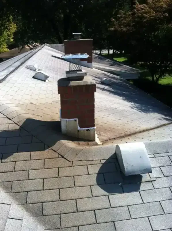 Roof with multiple brick chimneys and metal vents in daylight
