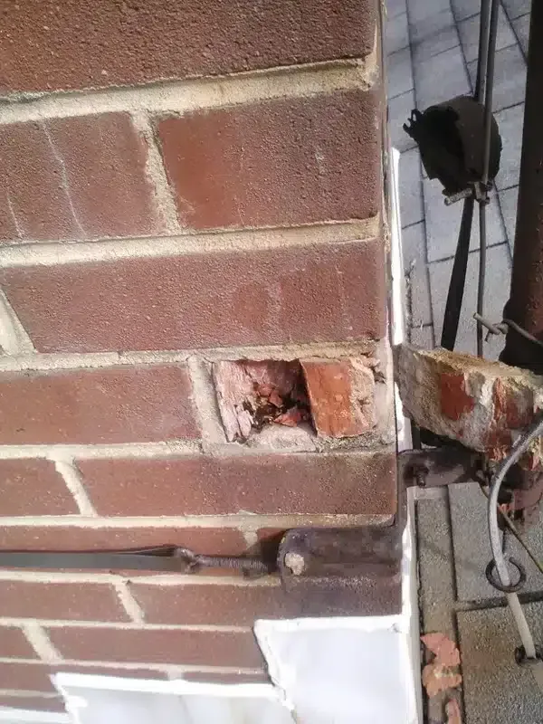 Damaged brick wall with a missing section and exposed brick near a metal gate
