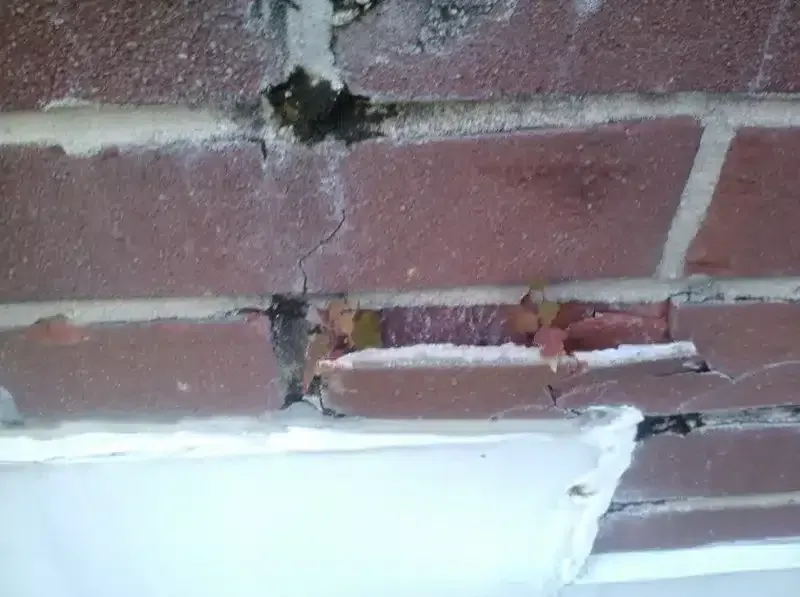 Cracked red brick wall with a damaged white ledge or sink at the bottom