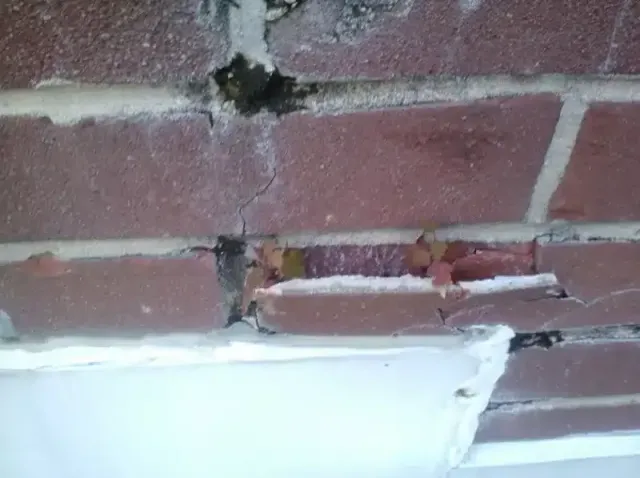 Cracked brick wall above a white bathtub or sink with exposed pipe and damaged plaster