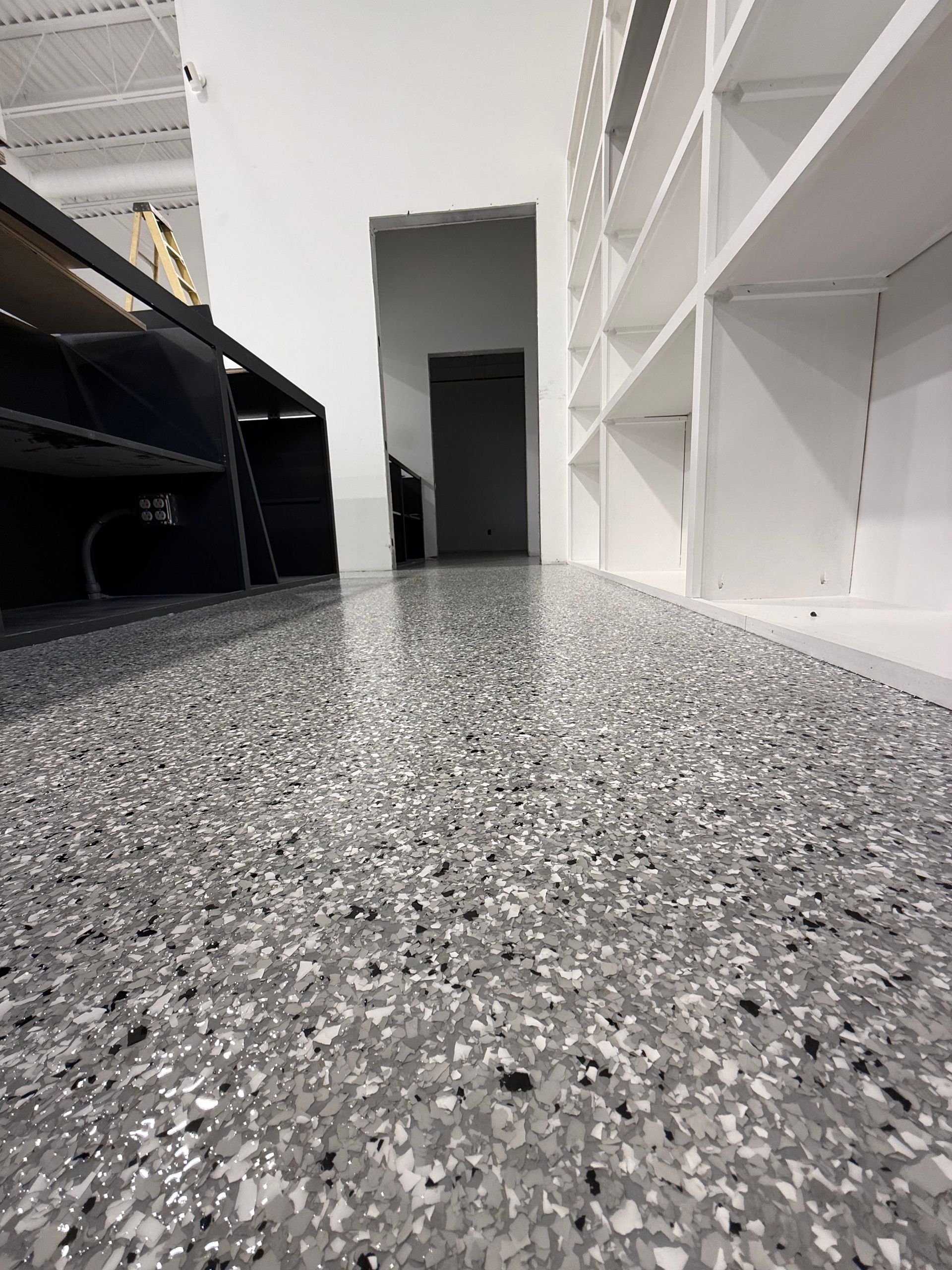 Low-angle view of a speckled countertop in a narrow kitchen with white shelves and a doorway.