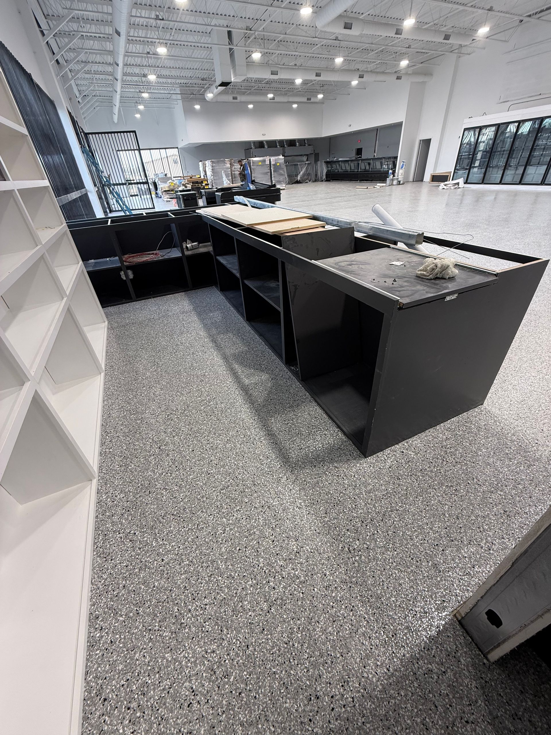 Empty modern kitchen with black counters, stainless appliances, and speckled gray floor.