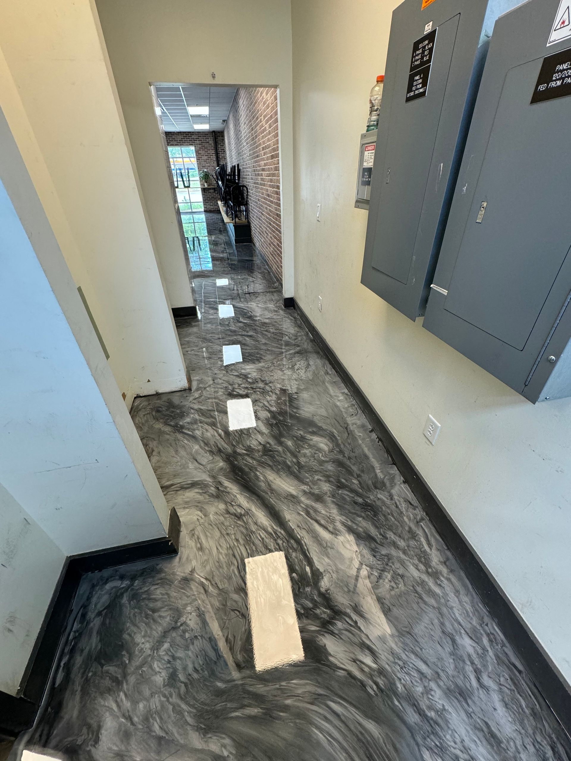 Hallway with unfinished dark floor, white walls, electrical panels, and exposed flooring patches
