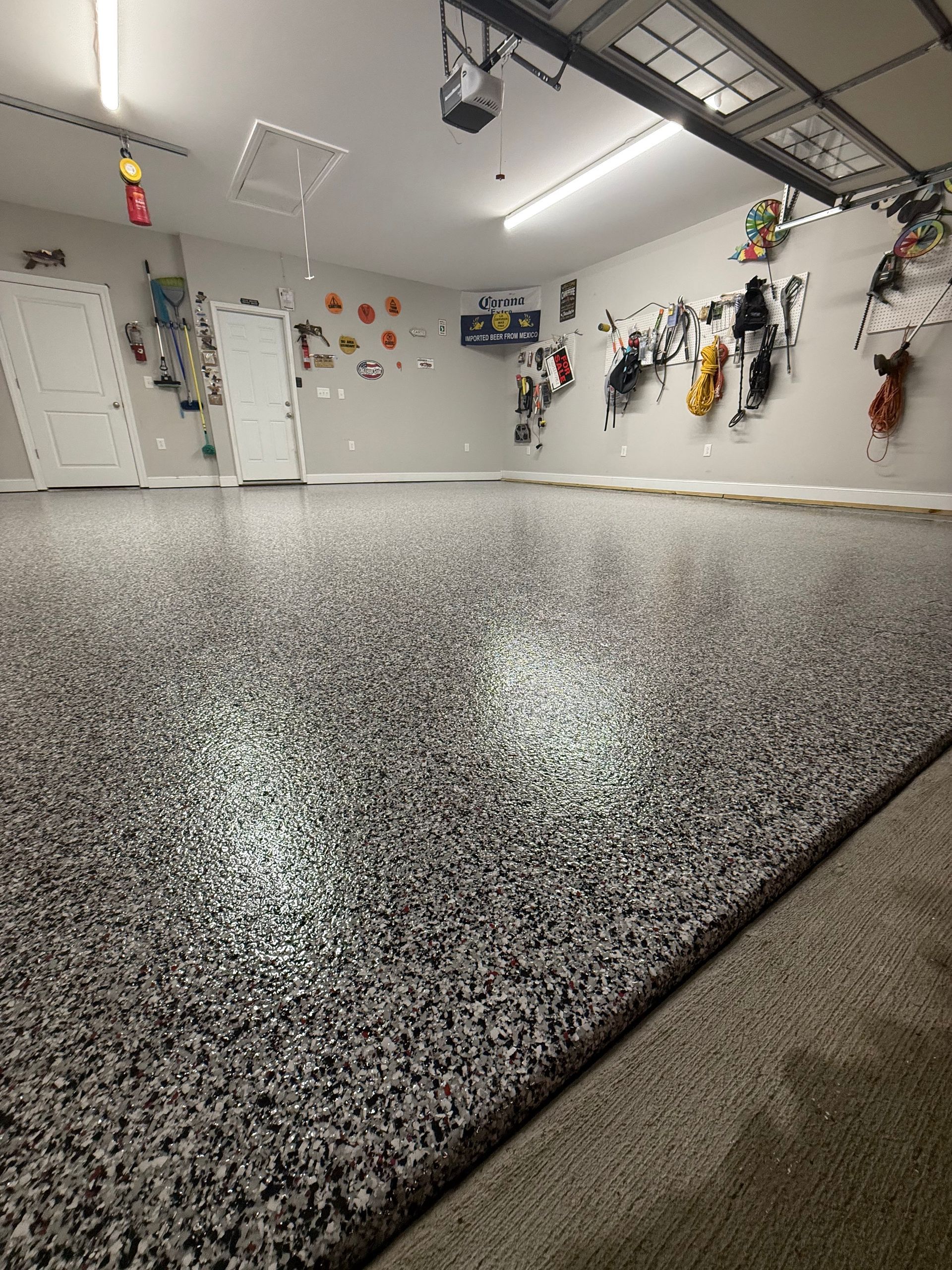 Empty garage with speckled gray floor and wall-mounted tools under bright overhead lights