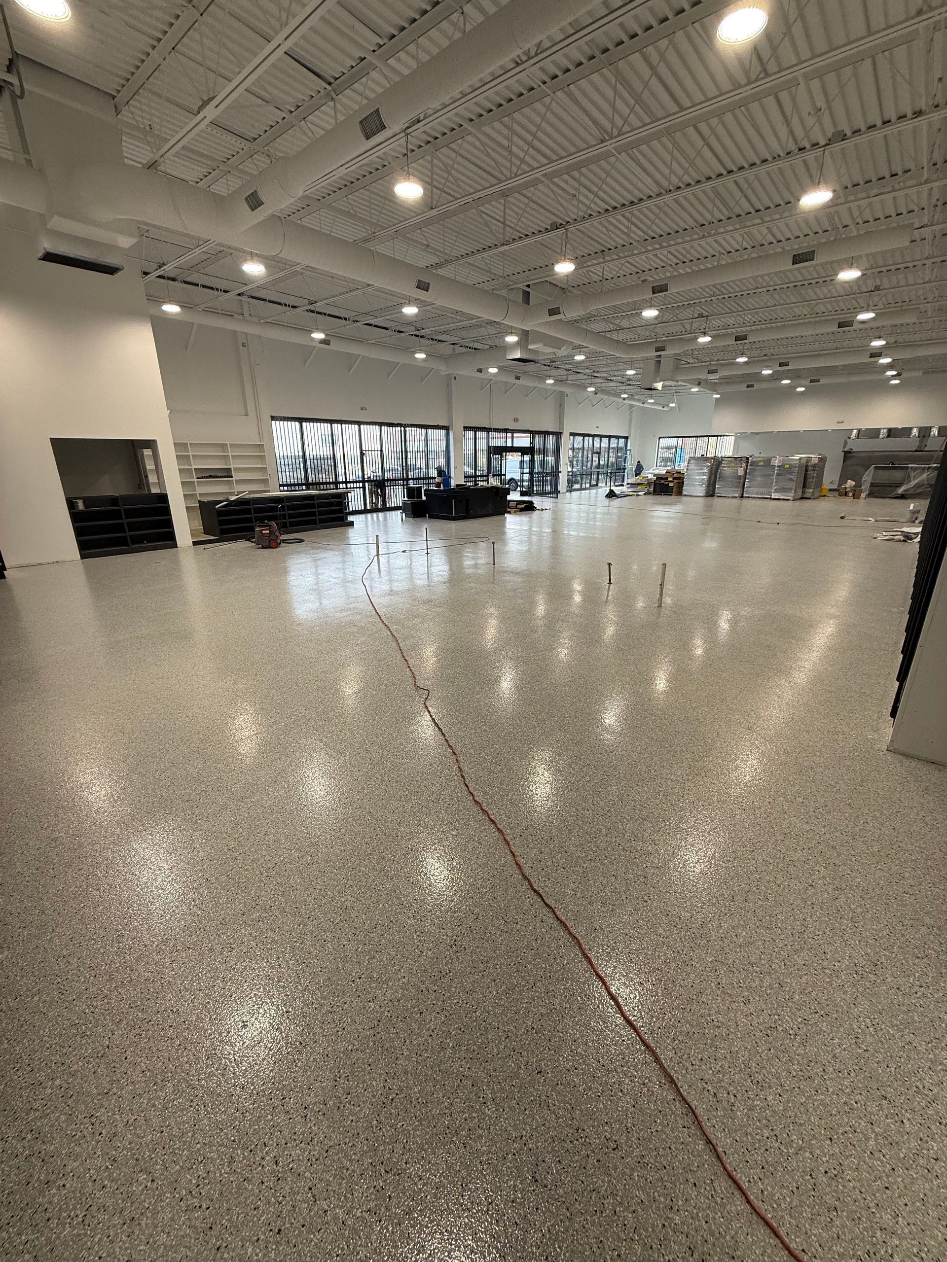 Empty indoor showroom with polished concrete floor, bright ceiling lights, and windows along one wall
