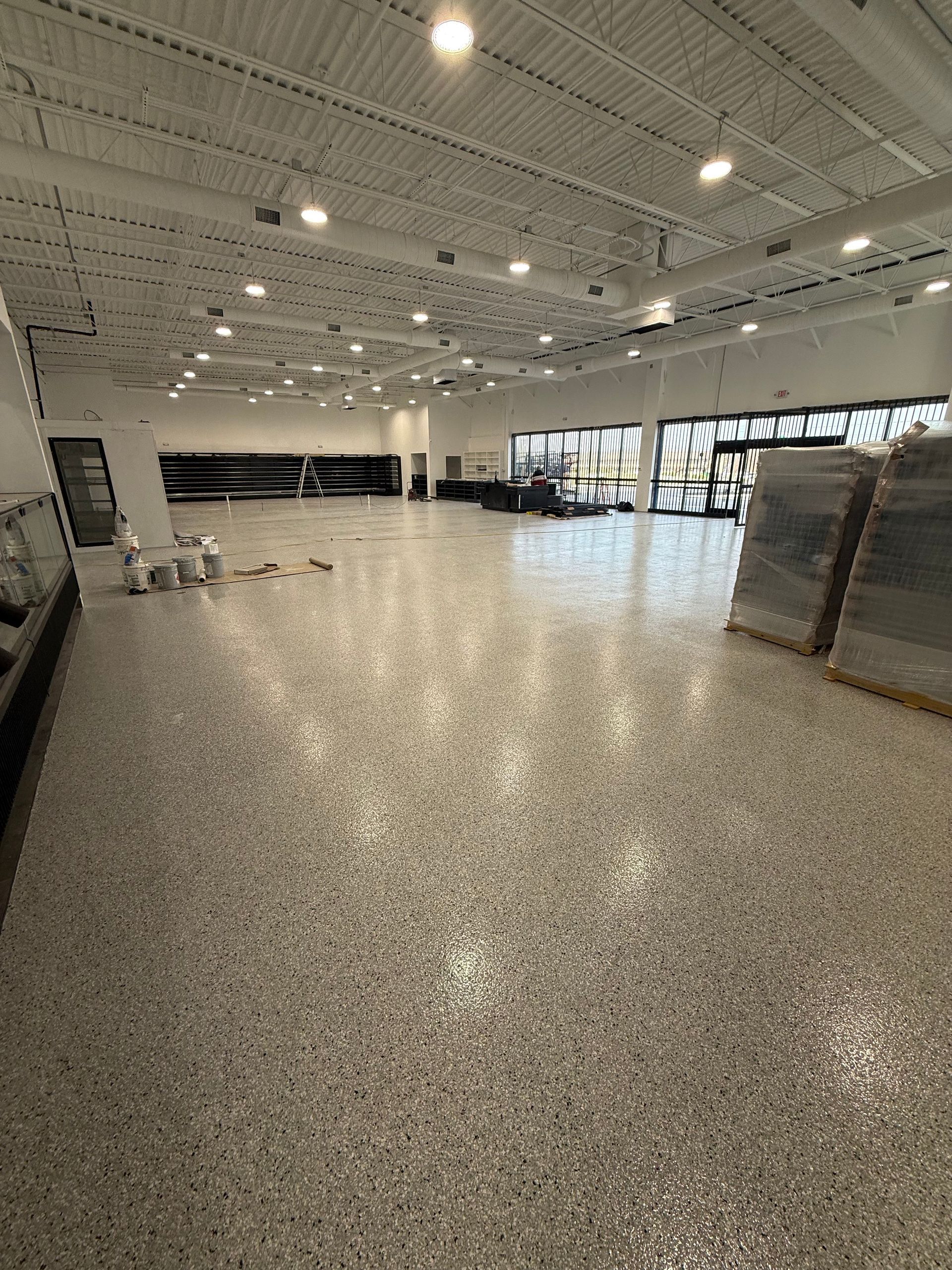 Empty retail showroom with glossy speckled floor, white ceiling lights, and windows along the back wall
