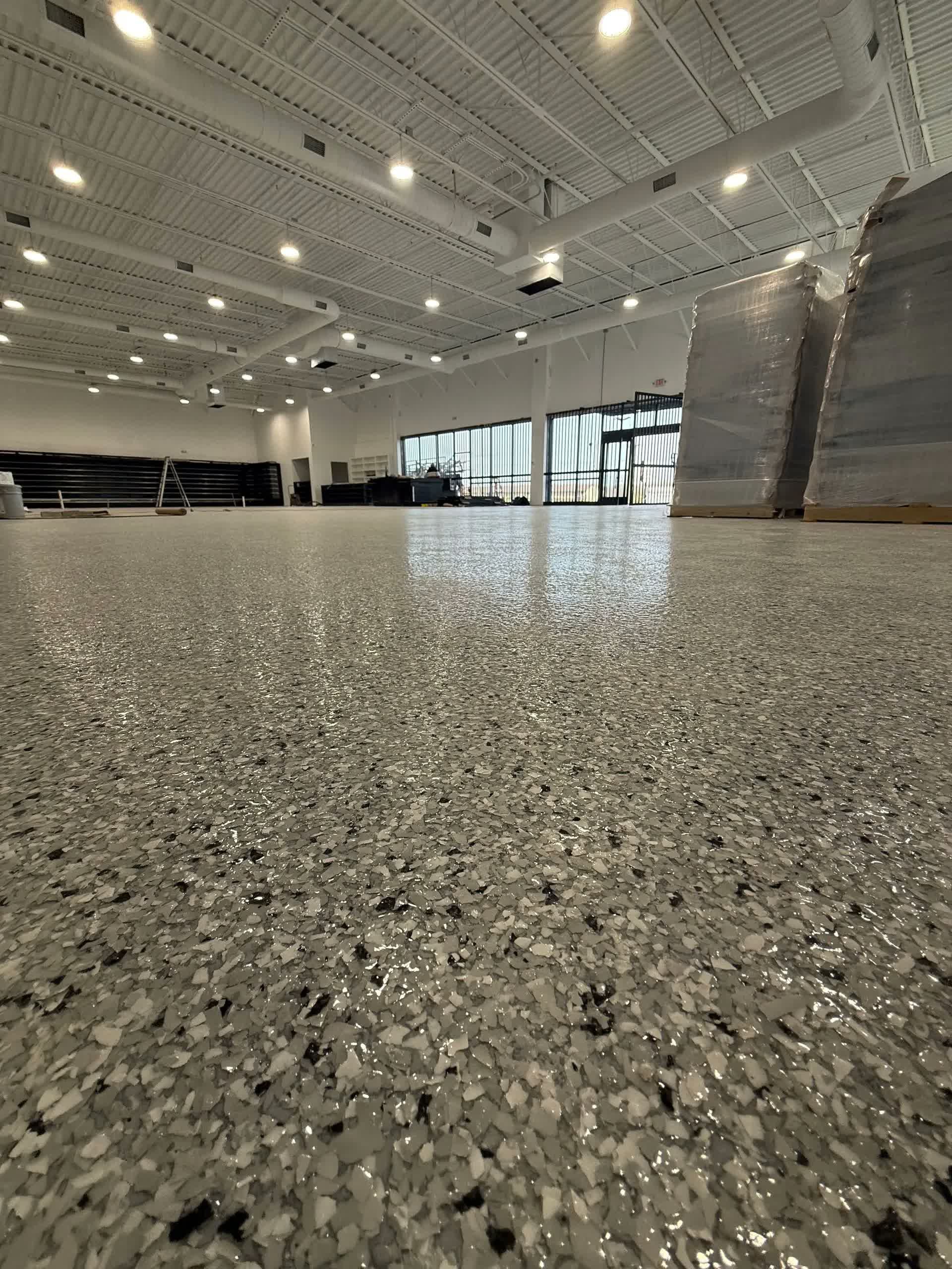 Spacious hall with a glittering textured floor, high ceiling lights, and large windows in the background