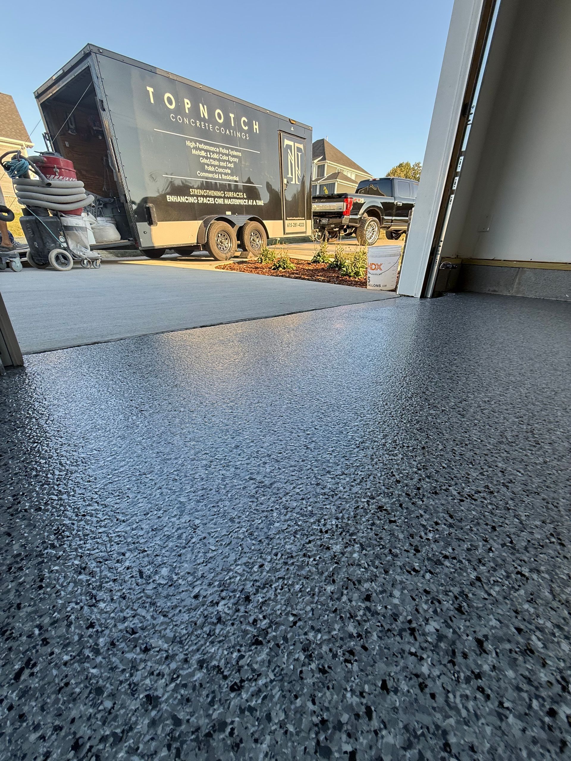 Speckled floor beside an open doorway, with a truck and landscaping equipment outside in daylight