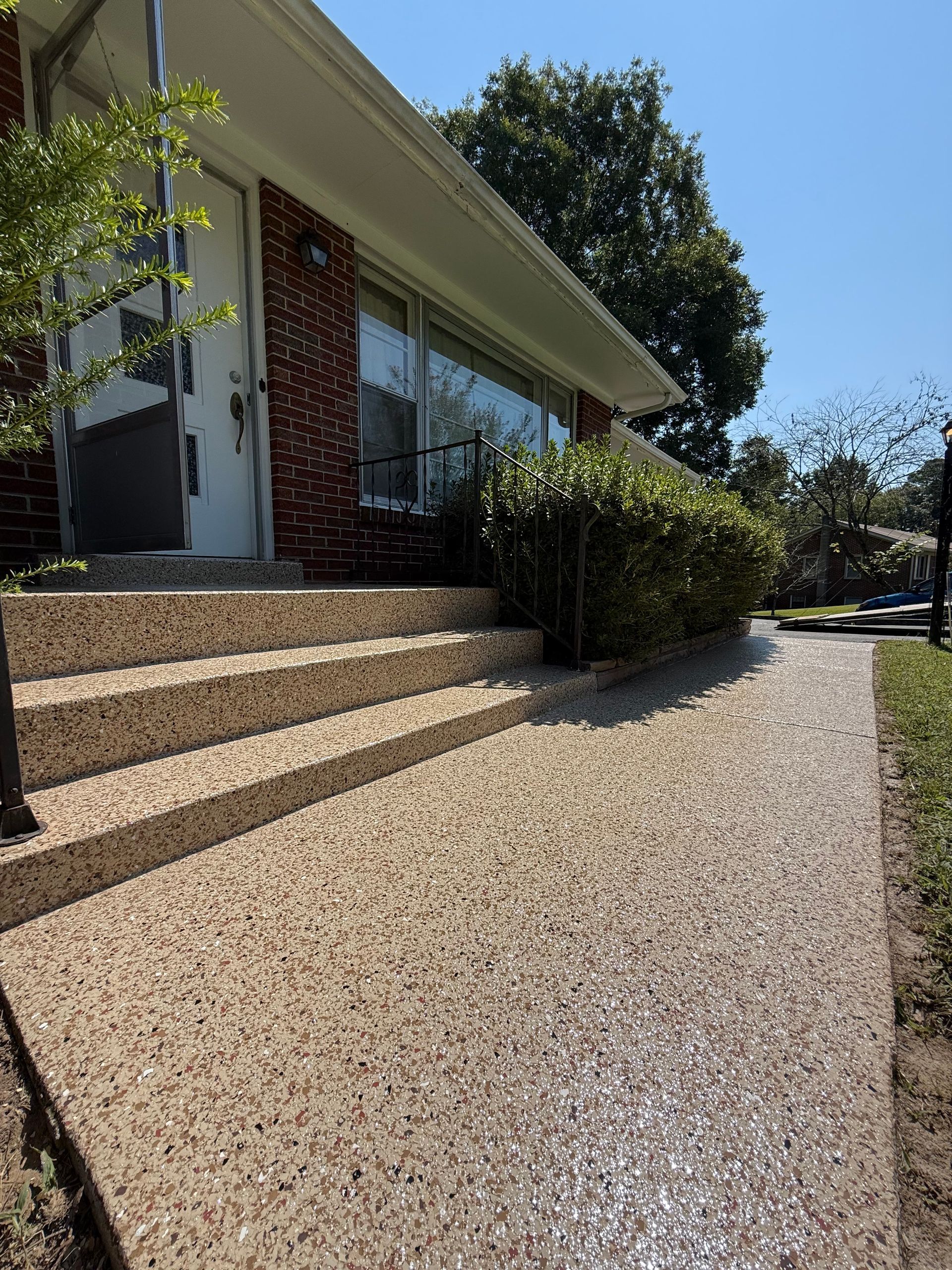 Modern house exterior with gravel driveway, steps, and hedges under bright sunlight