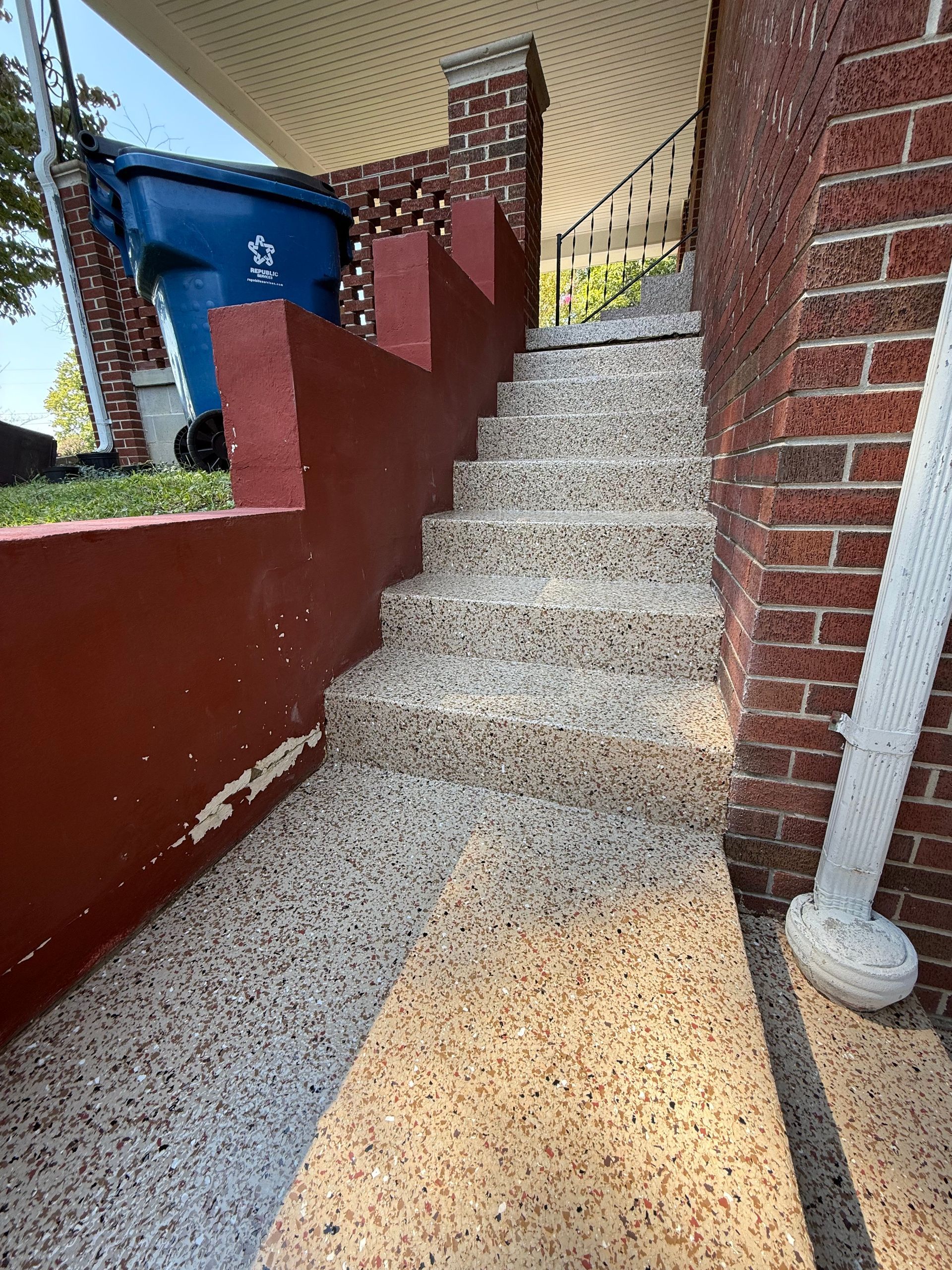 Narrow outdoor concrete stairway between red brick walls and a blue door, viewed from the bottom.