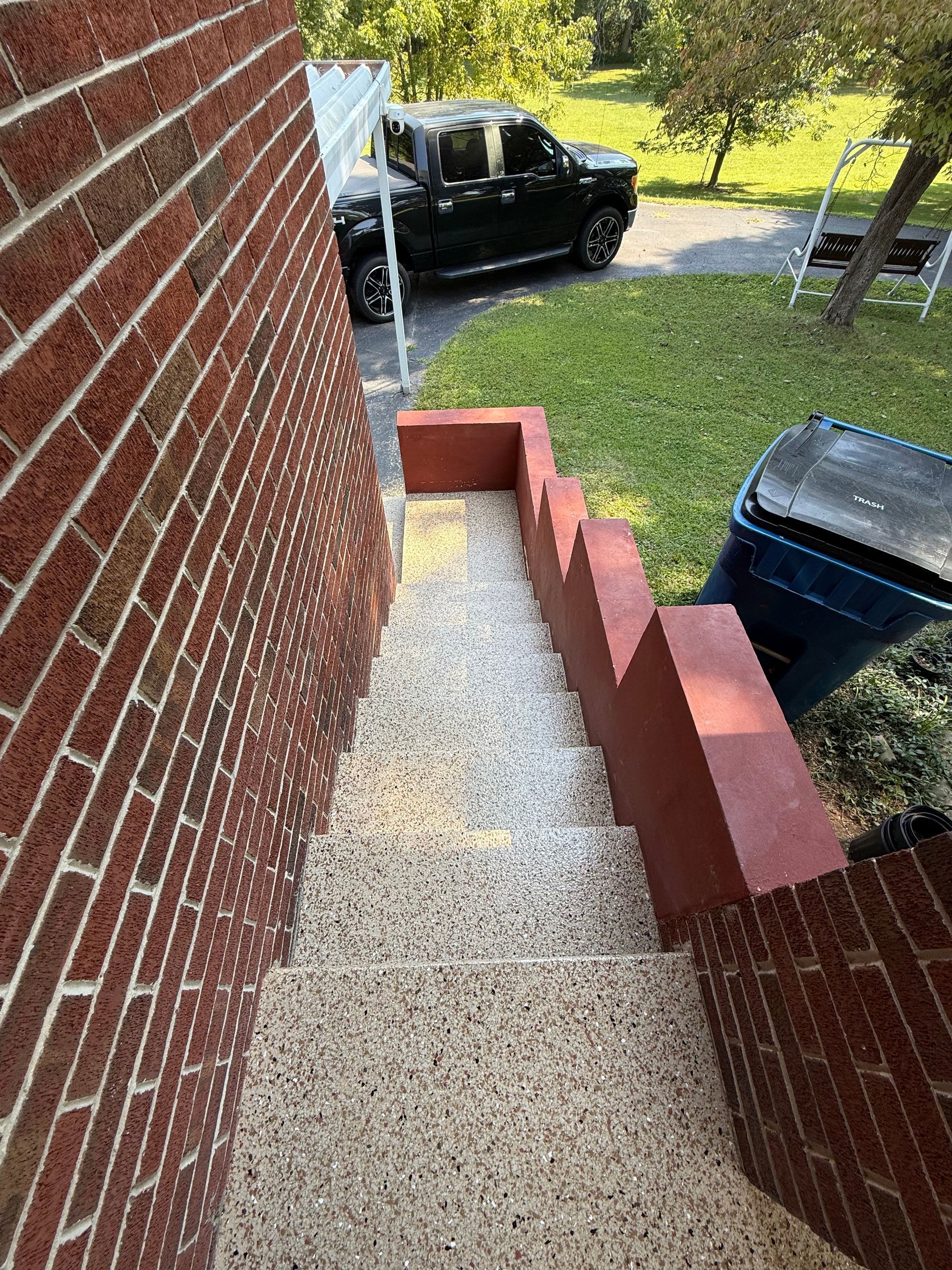 Concrete front steps beside a brick house, with a black SUV and trash bin at the bottom.