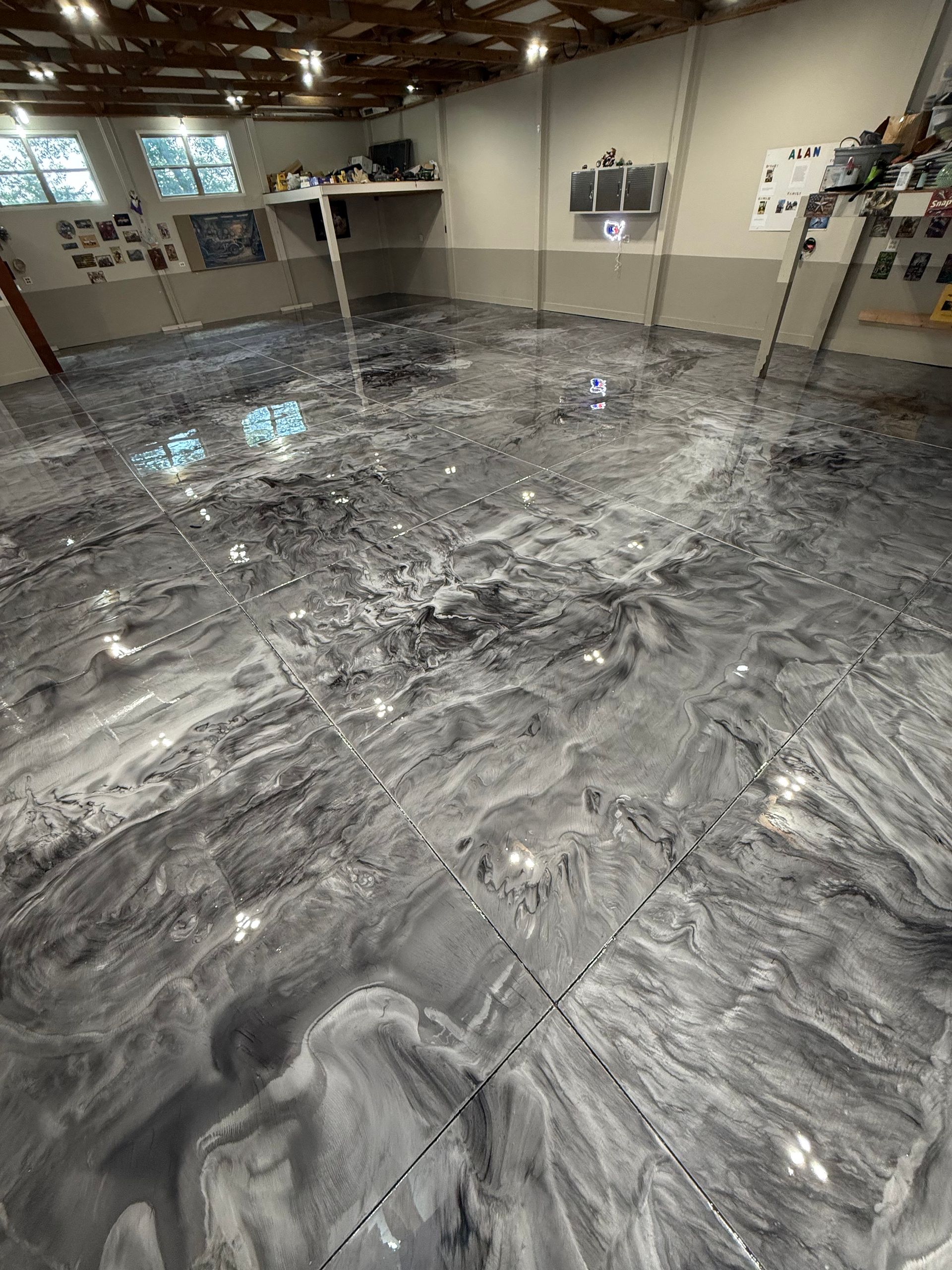 Basement floor coated in glossy gray epoxy with swirling marbled patterns under bright lights