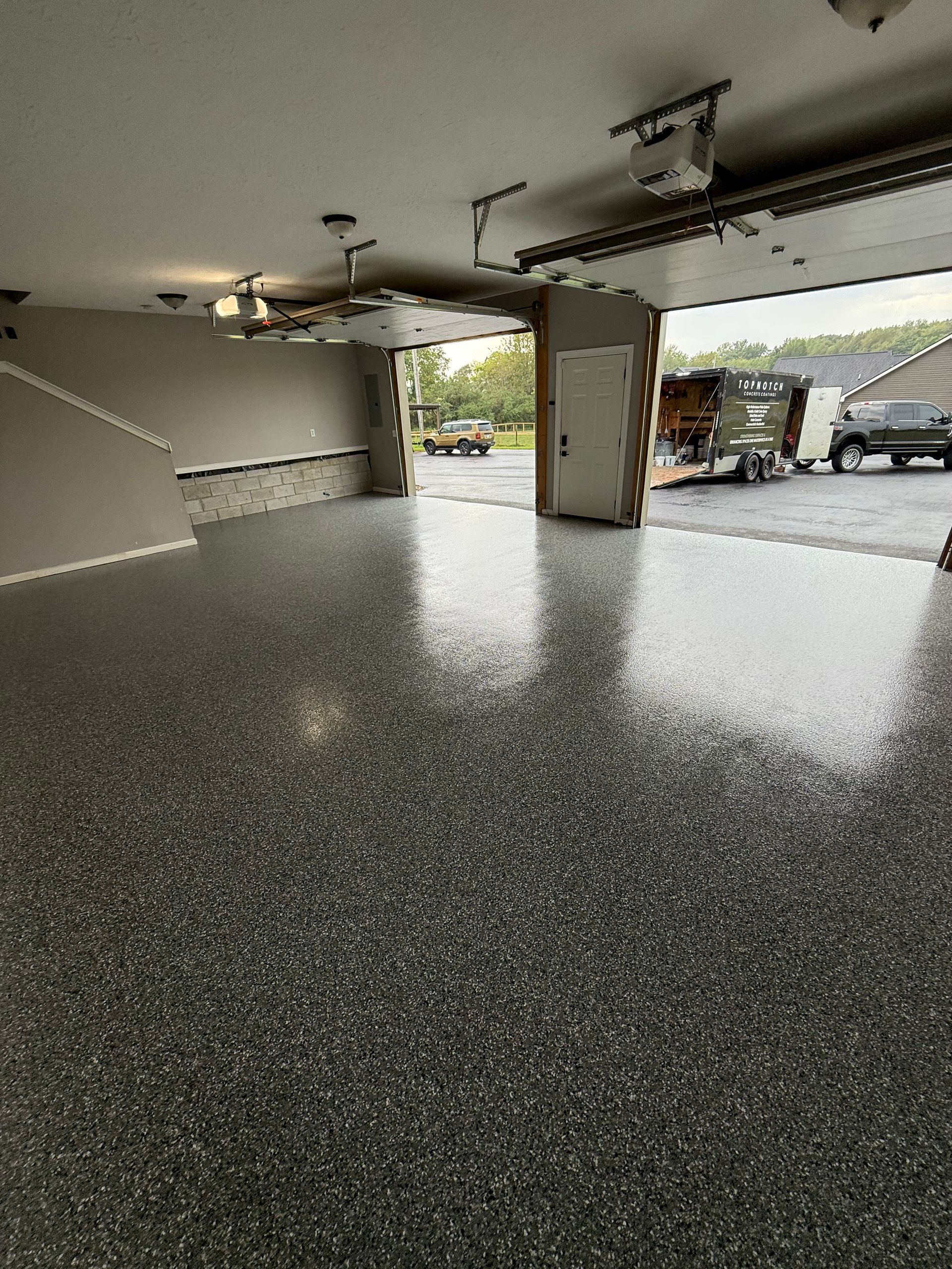 Spacious empty garage with speckled epoxy floor and open doors showing daylight outside