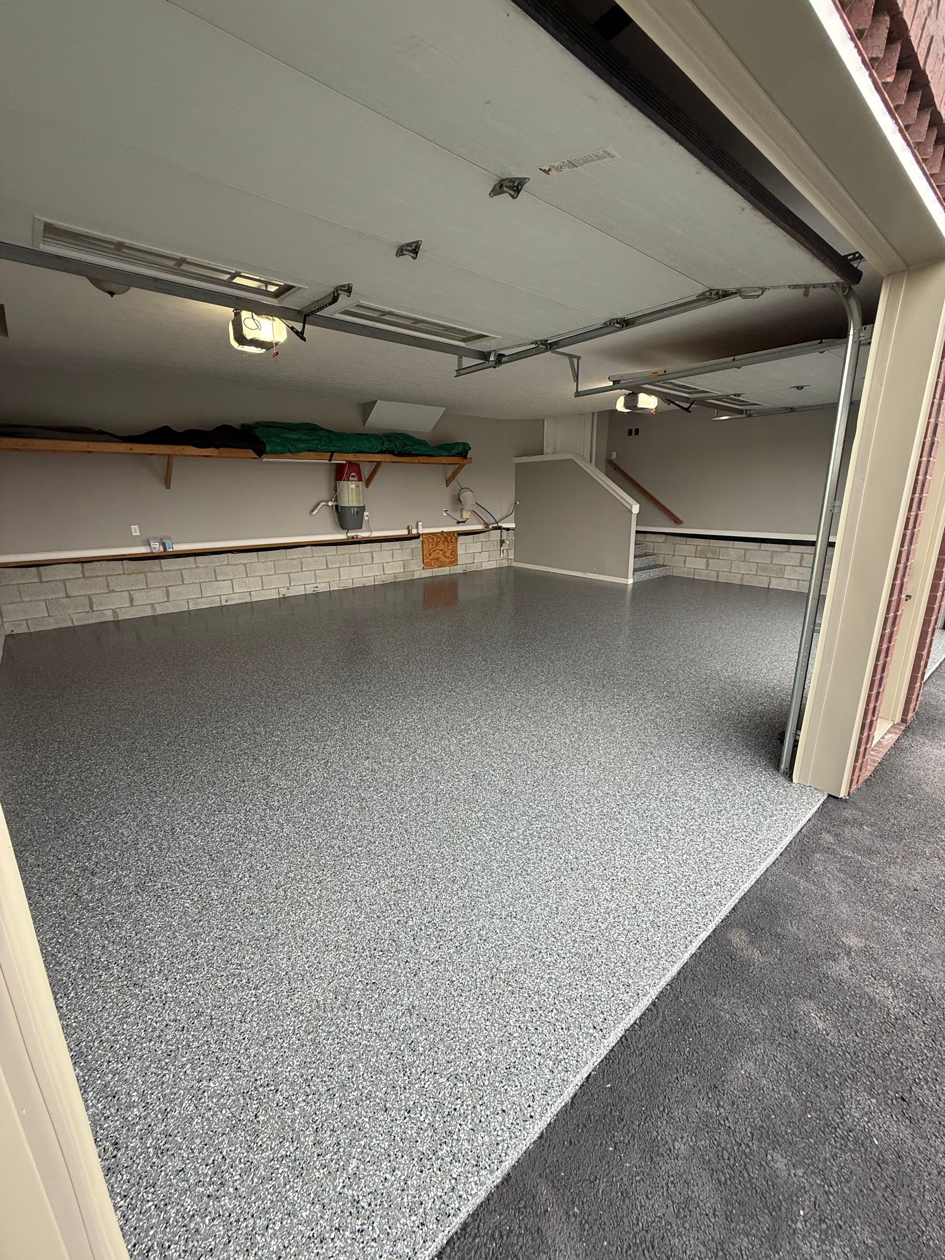 Empty garage with speckled gray floor, white walls, overhead lights, and open doorway.