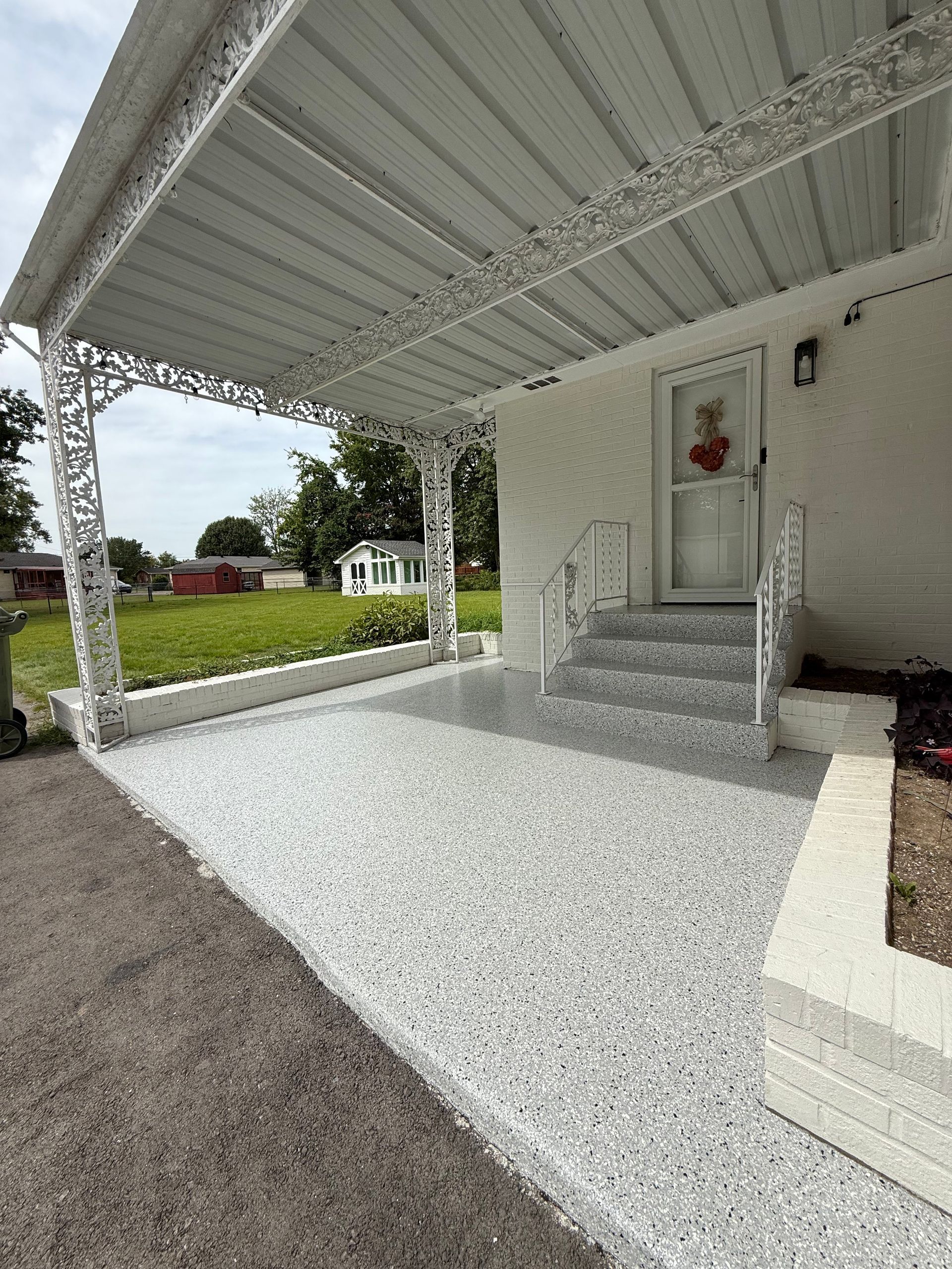 Covered front porch with white steps, ornate railings, and gravel driveway beside a house.