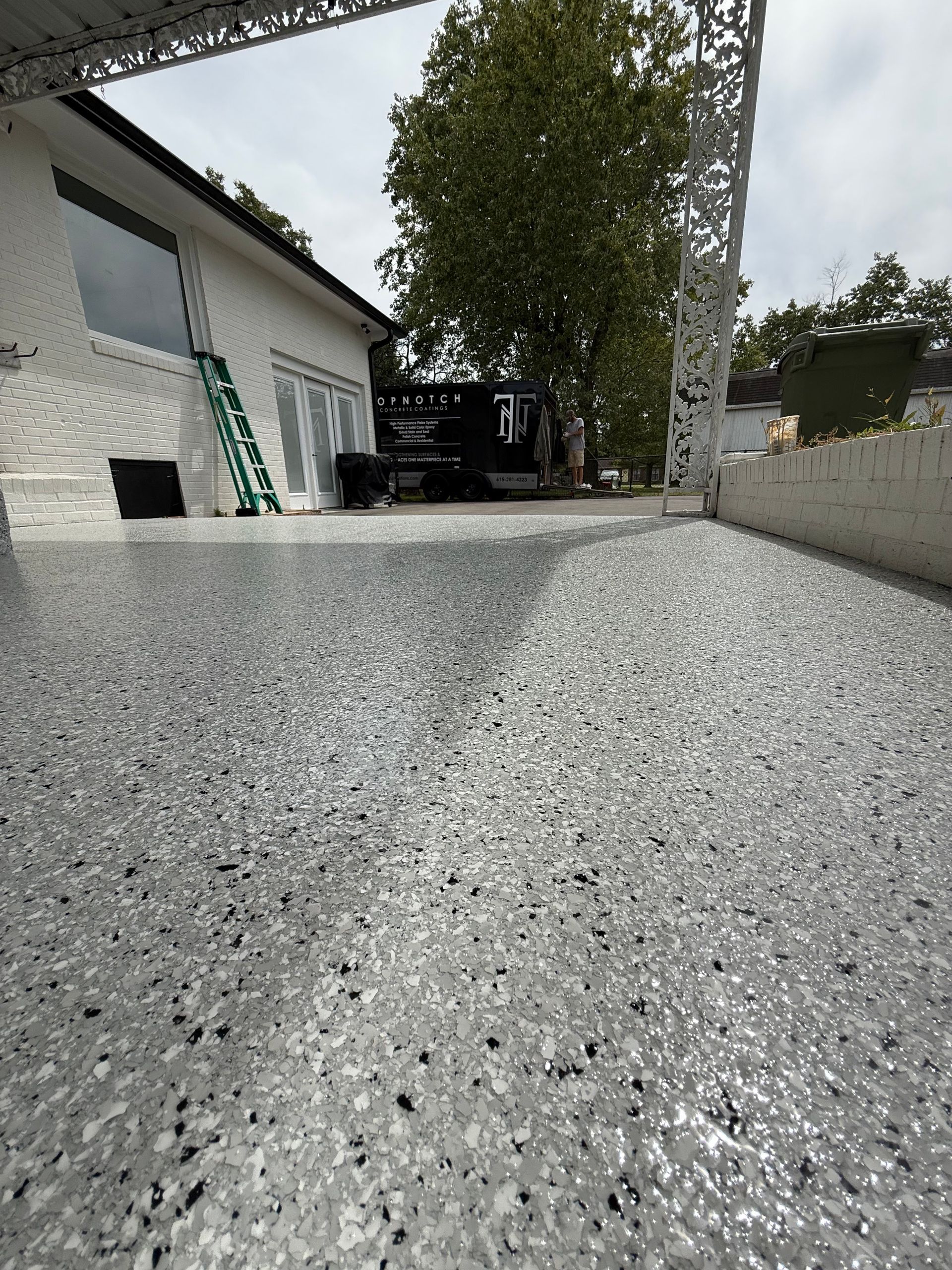 Low-angle view of a gravel driveway beside a house, with a tree and parked vehicle in the background.