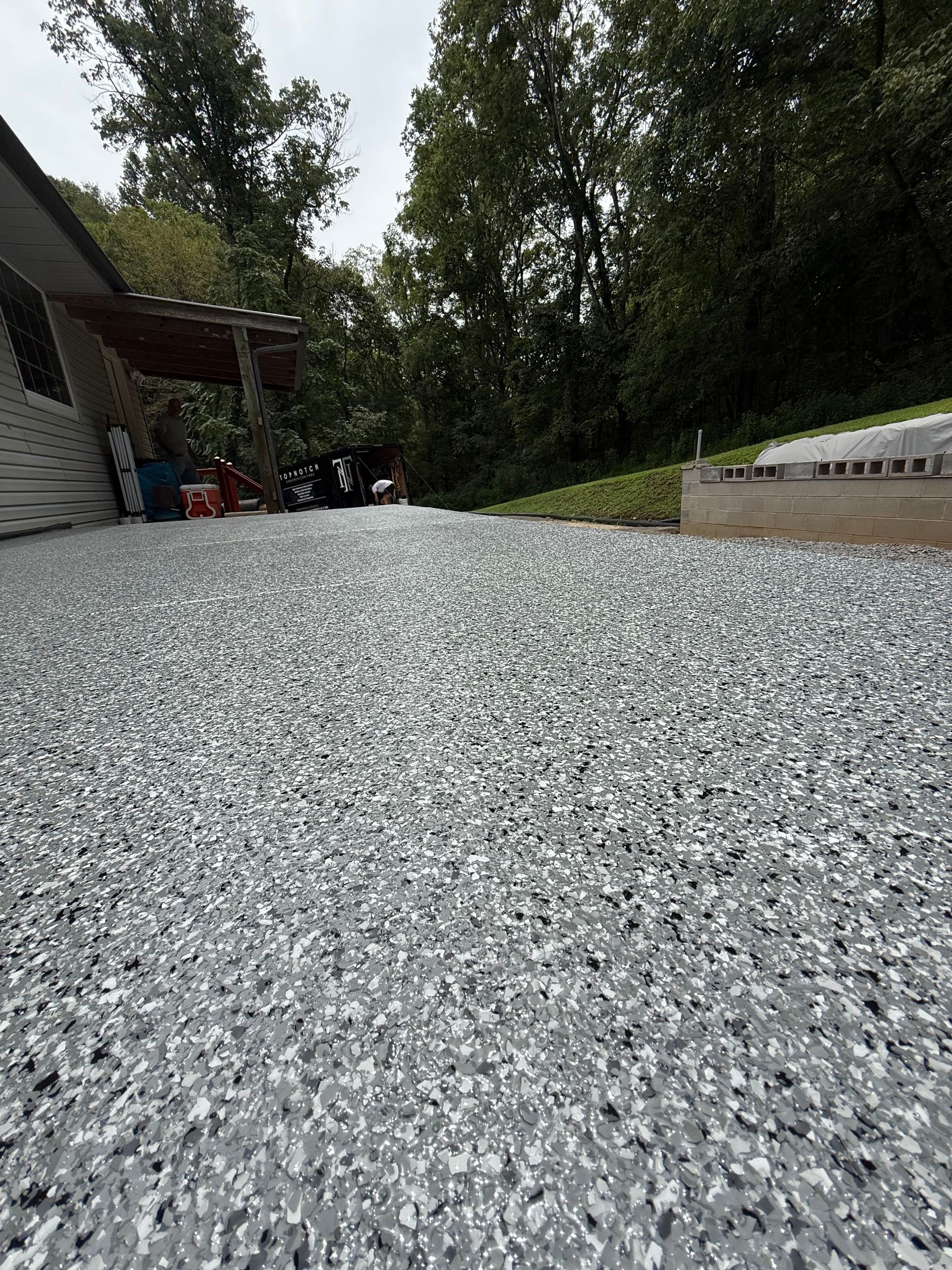 Gravel driveway beside a house, leading toward trees and a wooded area.