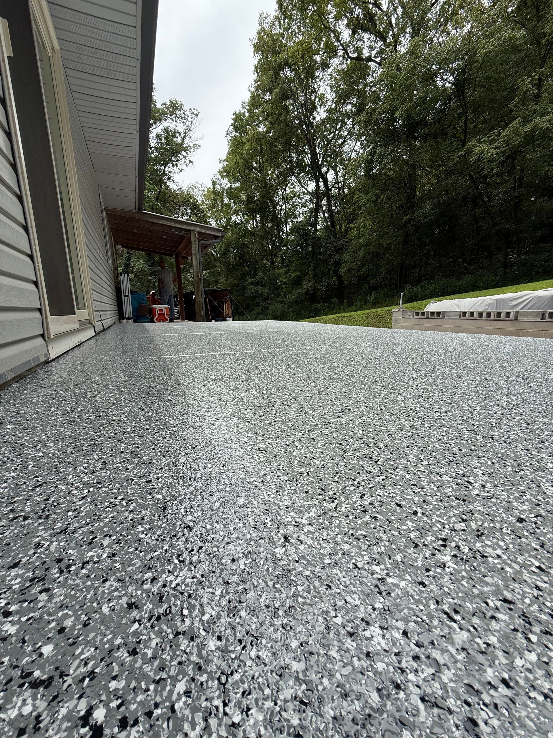 Gravel driveway beside a house, leading toward a covered porch and trees beyond.