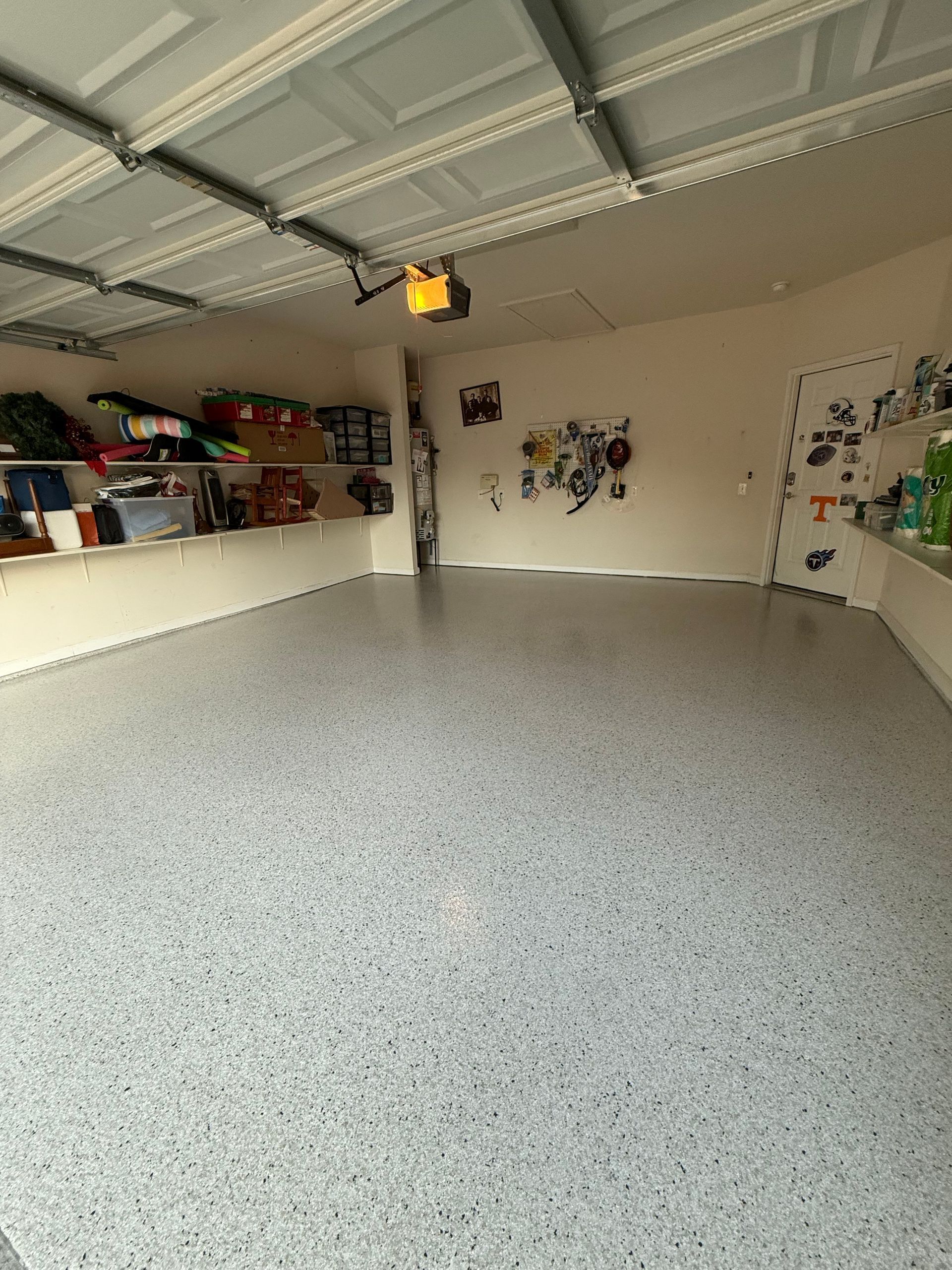 Empty garage with speckled floor, open shelves on the left, and a ceiling-mounted light.