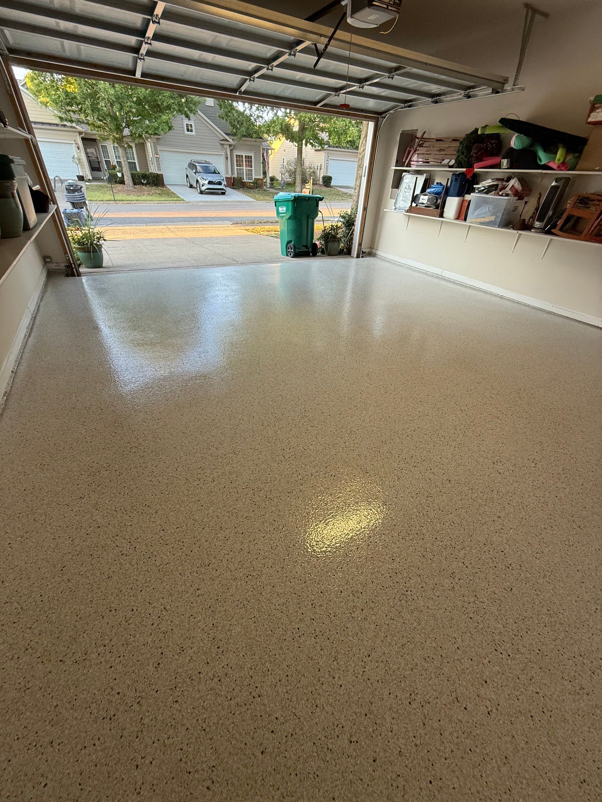 Empty garage with speckled floor, open door, and shelves along the right wall.