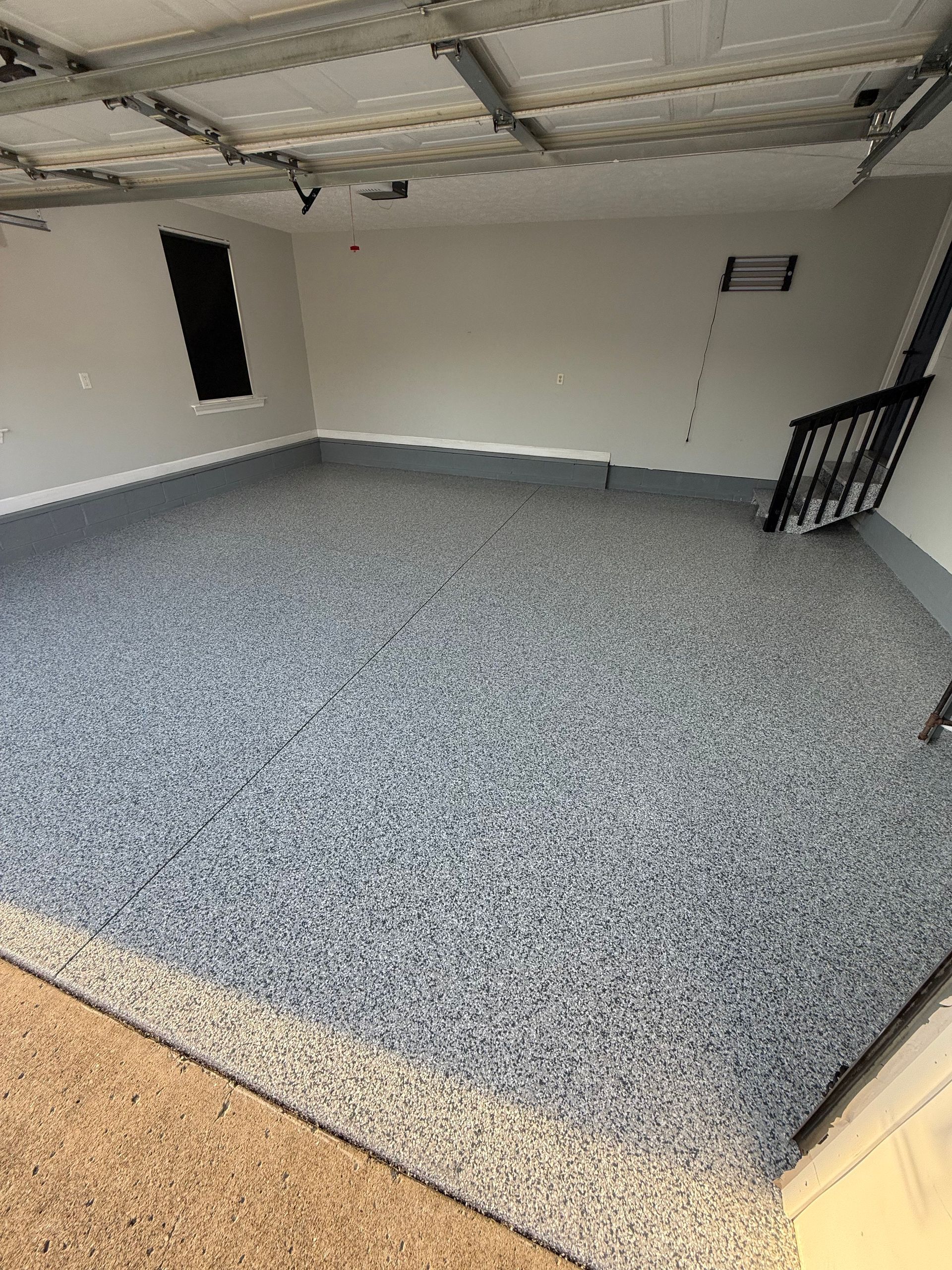 Empty garage with gray speckled floor, white walls, and an open door.