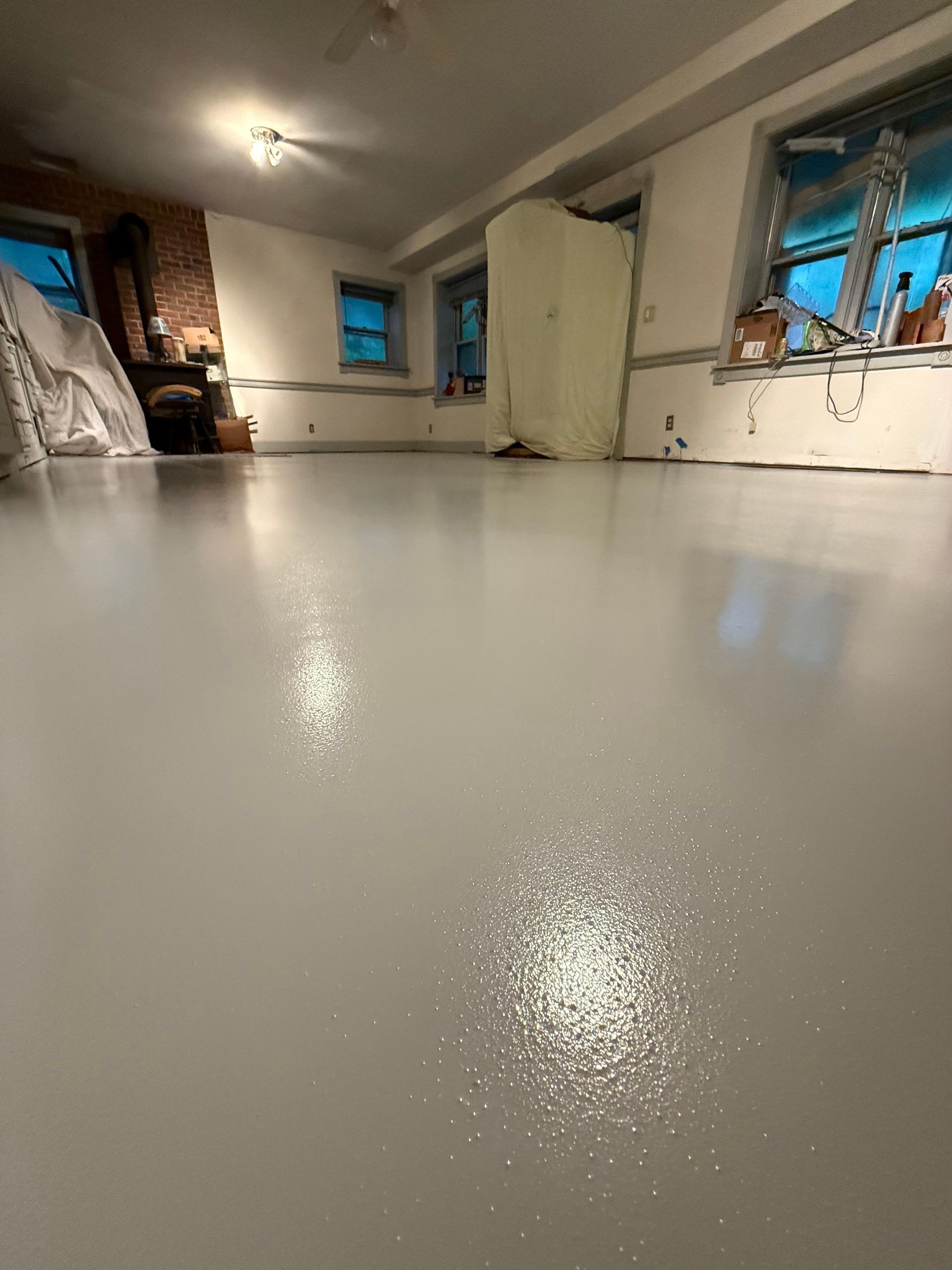 Shiny white resin floor in an unfinished room with windows and a fireplace alcove.