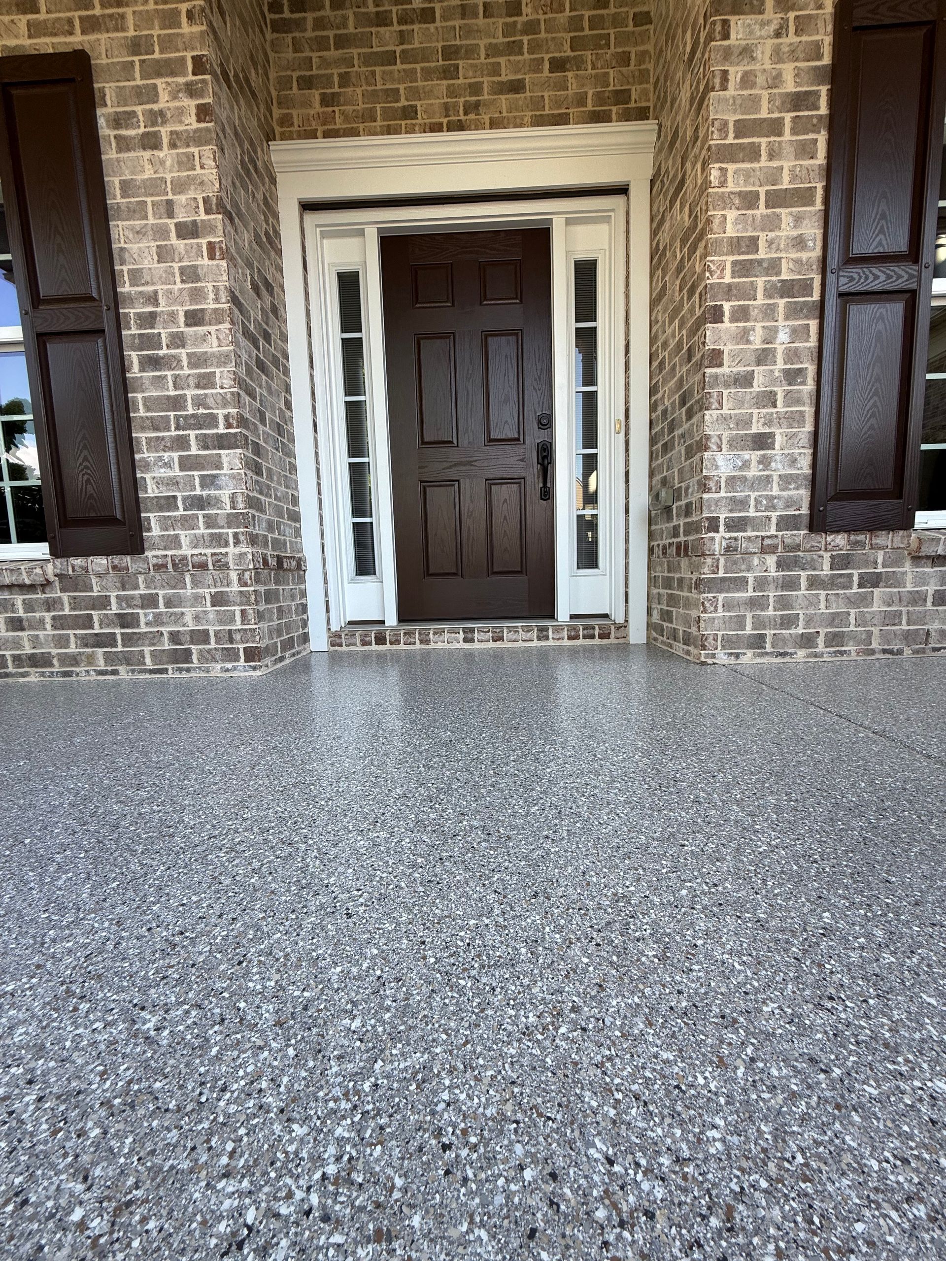 Brick house entryway with dark door, white trim, and speckled concrete porch