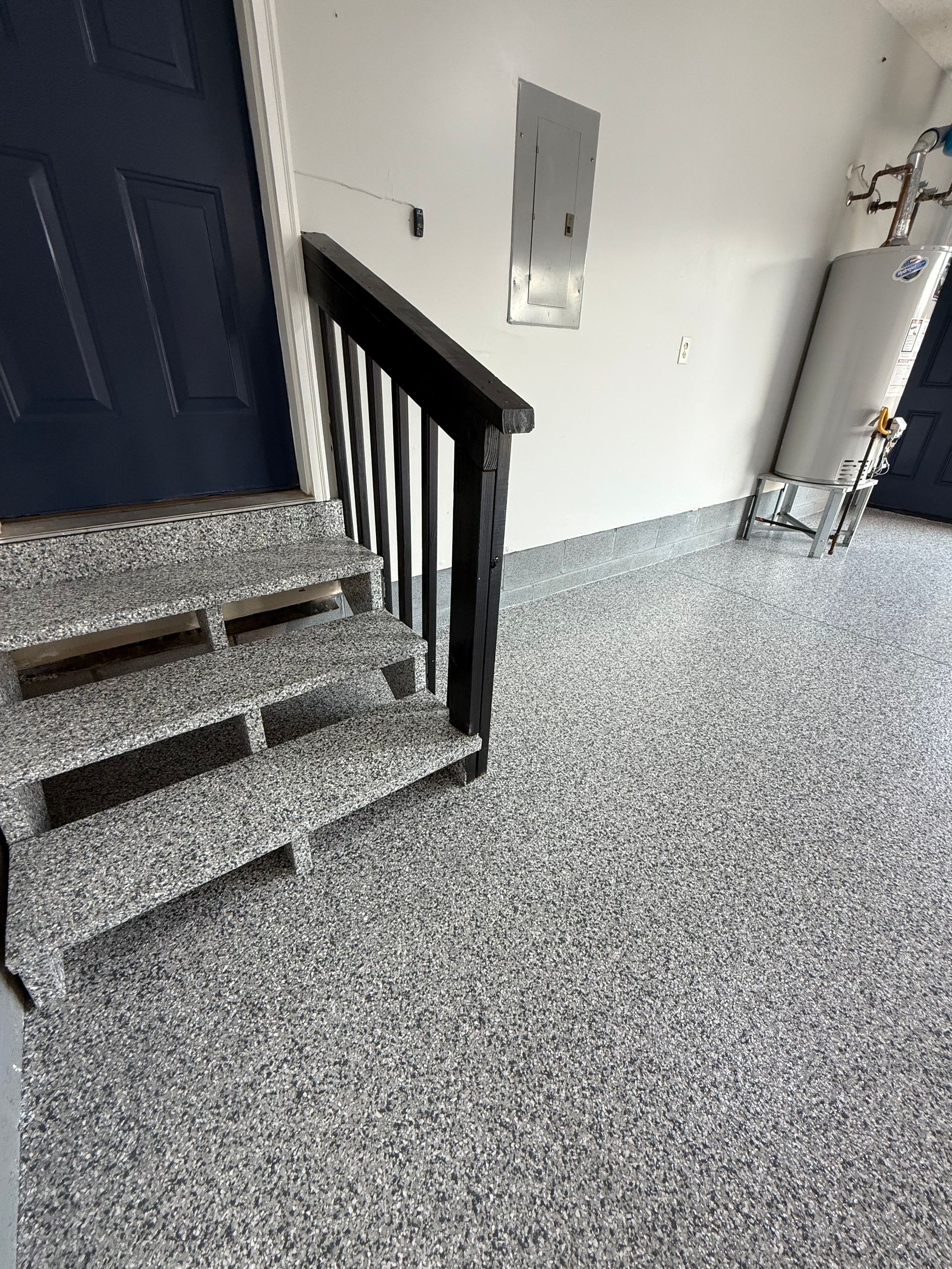 Interior stairway with black railing, blue door, and speckled gray floor and walls