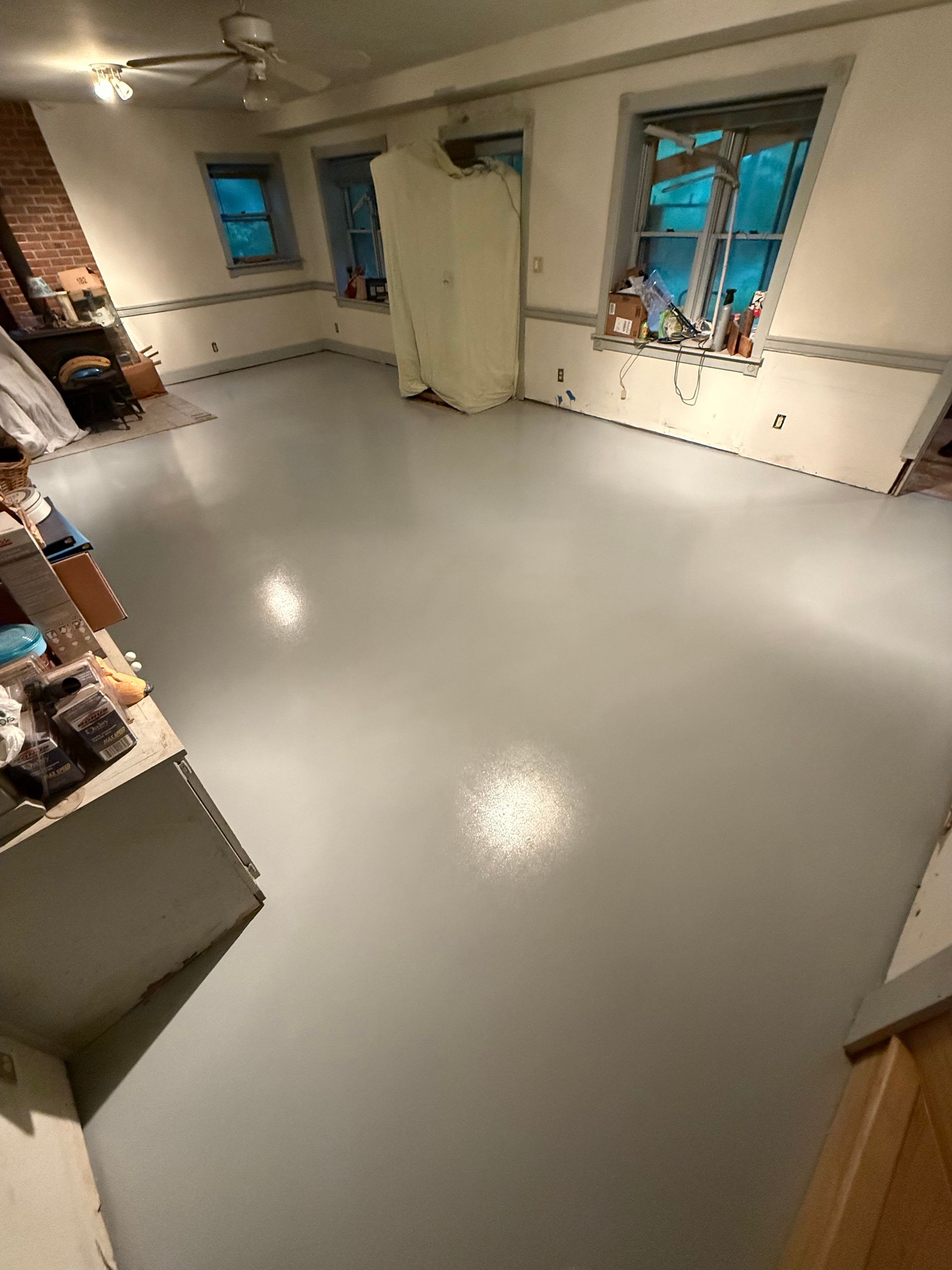 Empty white room with gray floor, windows, and a closed door under ceiling fans.