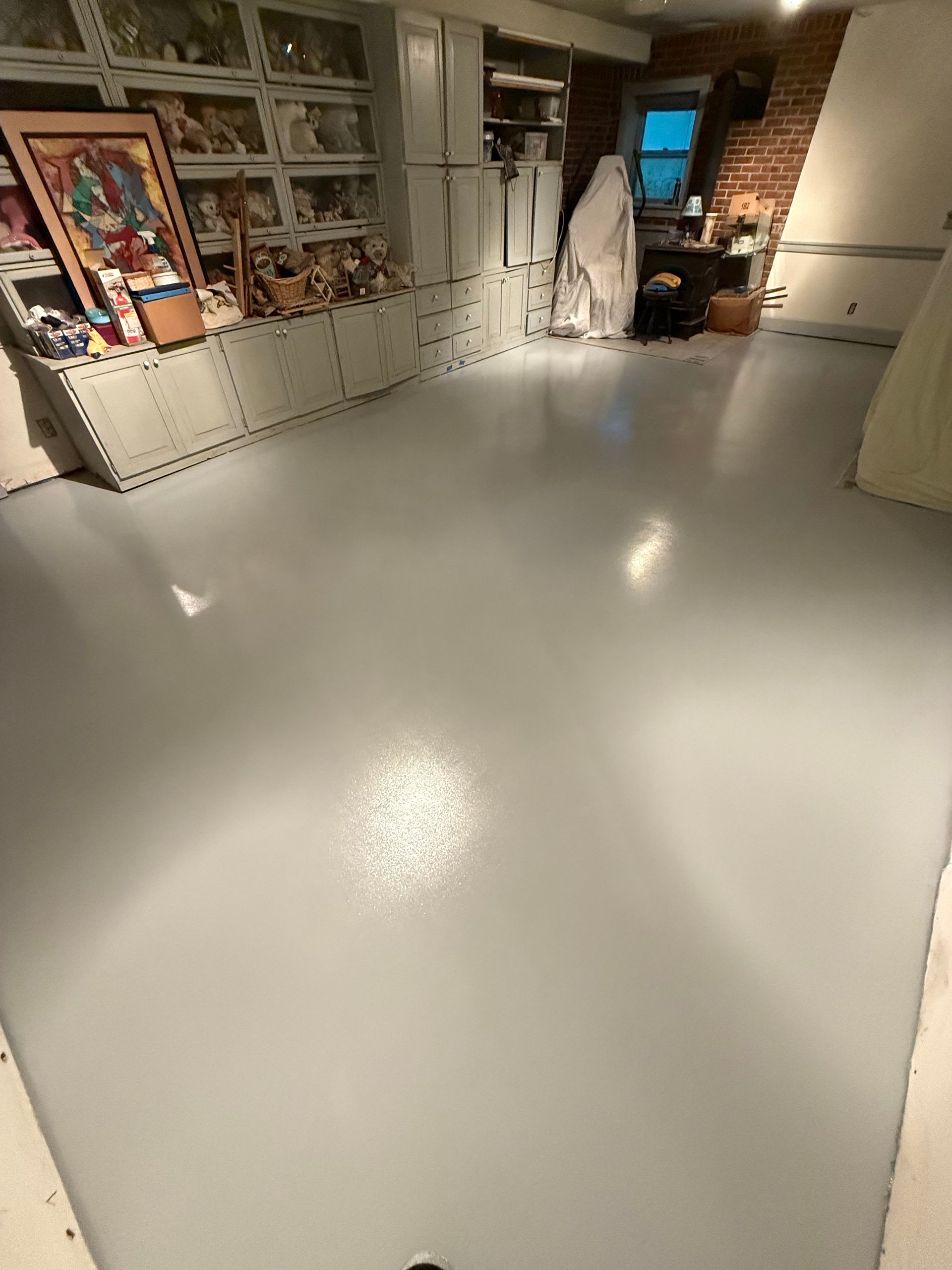 Bright gallery room with glossy white floor, framed art on the left, and lights reflecting on the surface.