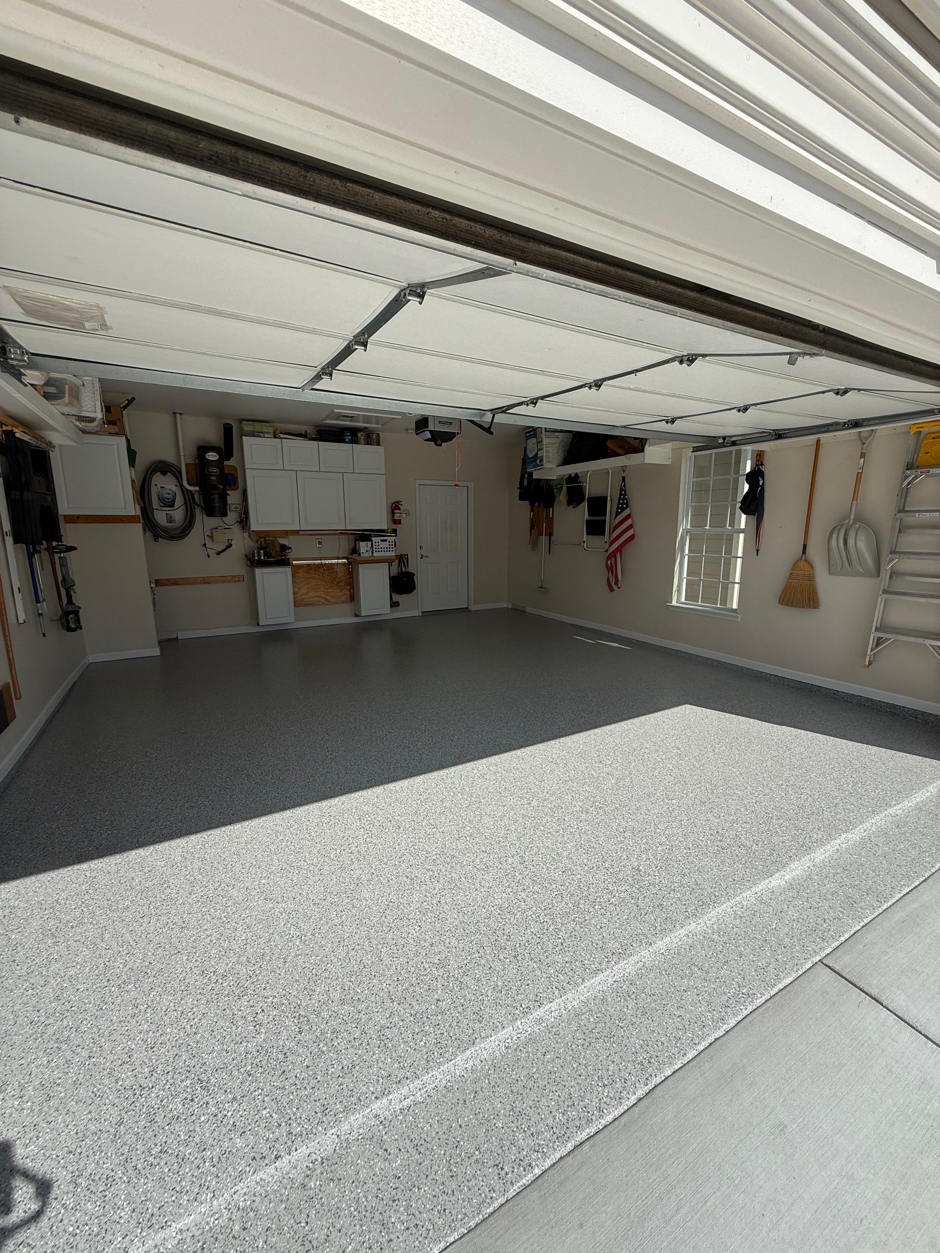 Empty garage with open door, speckled gray floor, and storage items along the walls.