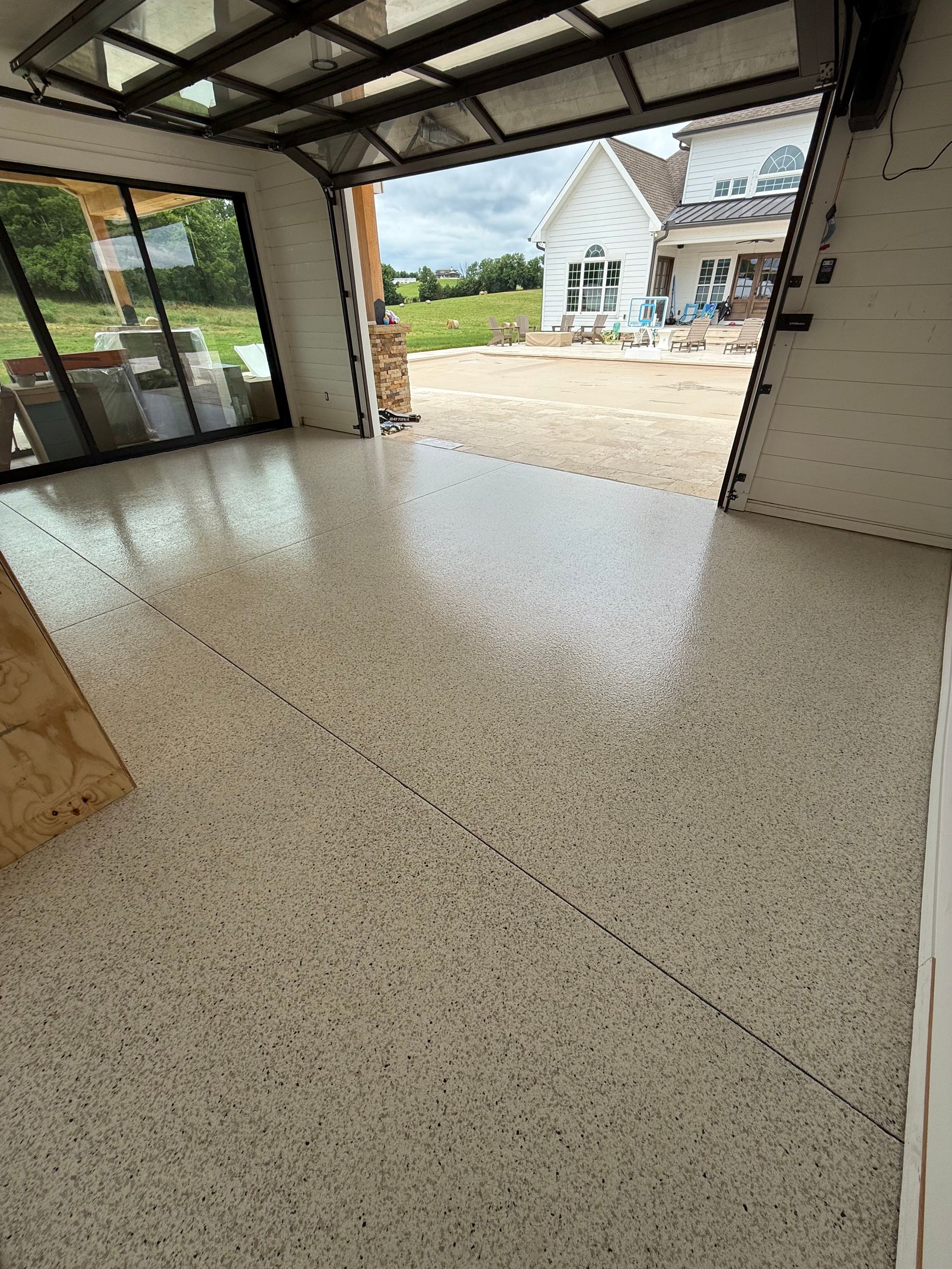Empty modern garage with speckled floor and open view to a driveway and house outside