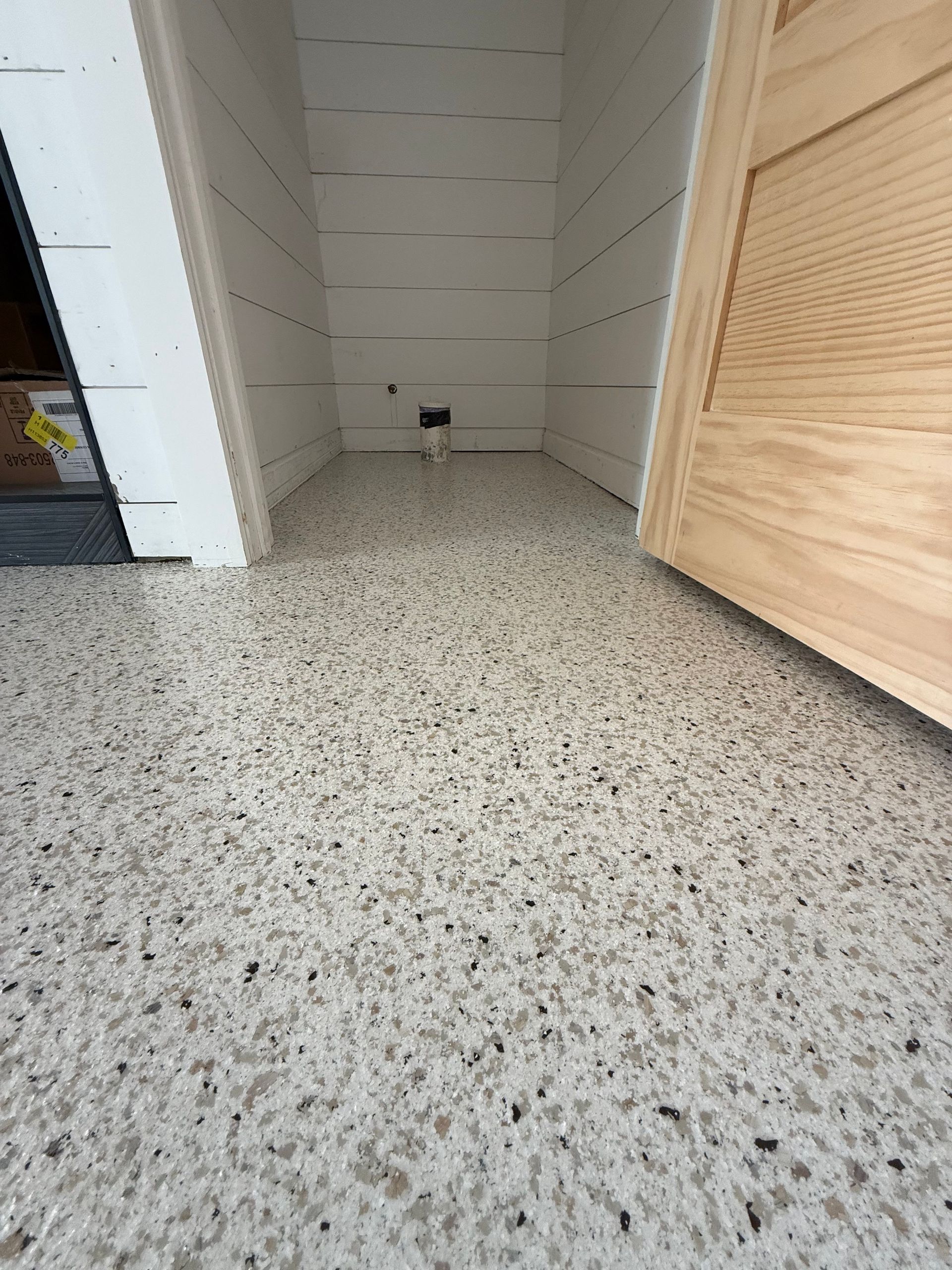 Empty white closet with speckled floor and wooden door ajar