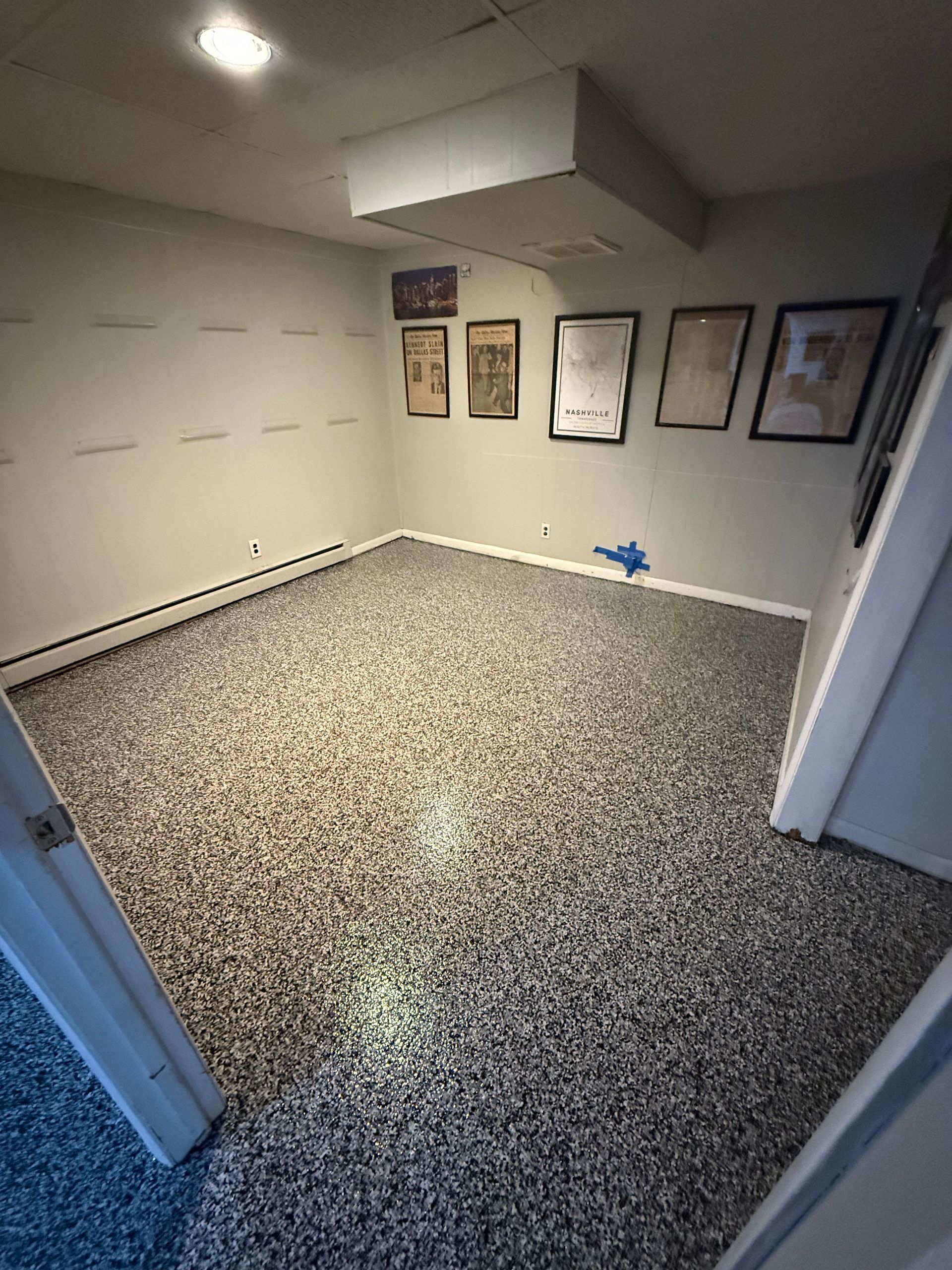 Empty carpeted room with gray walls, framed wall art, and a blue toy on the floor.