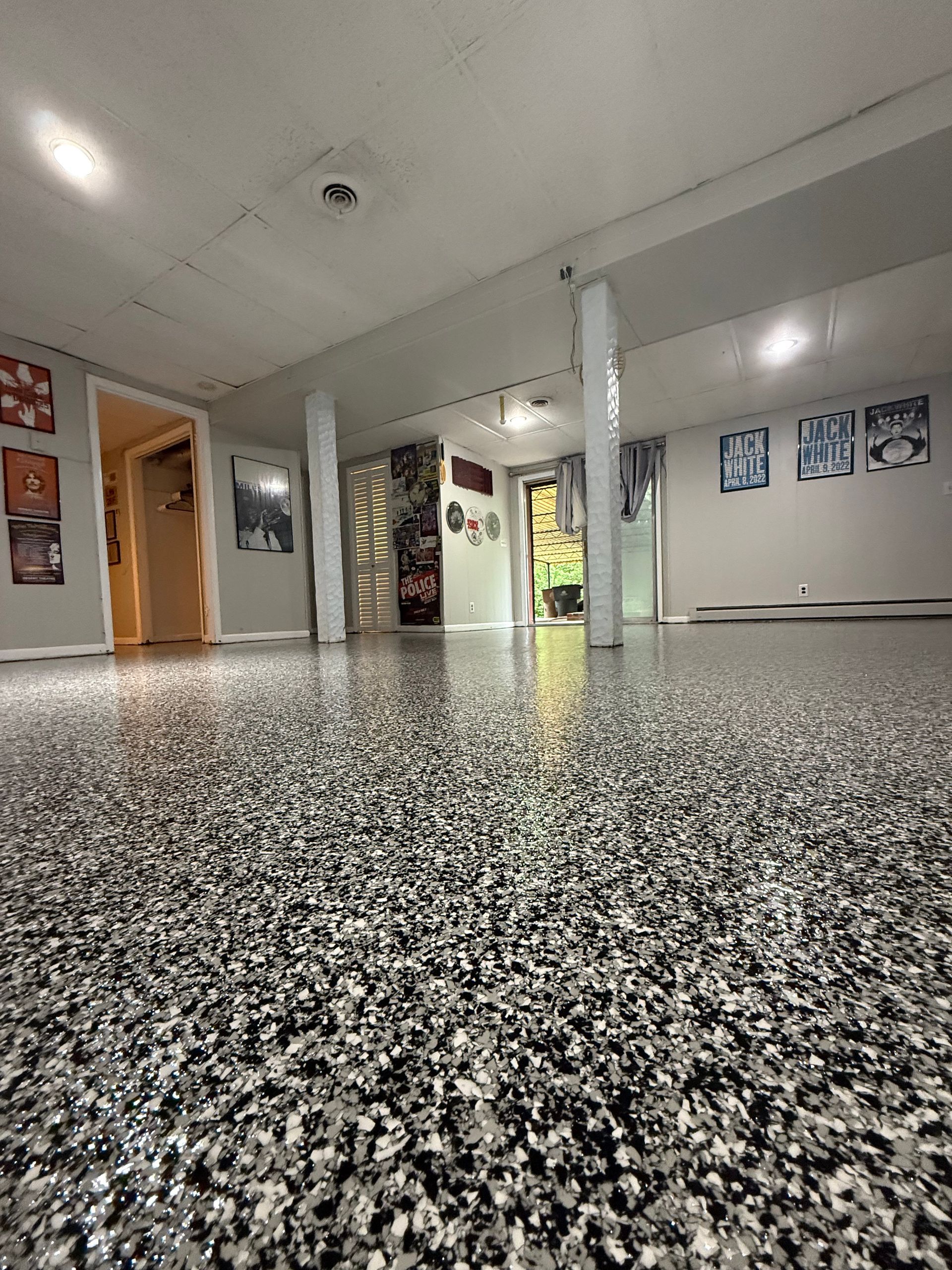 Empty indoor hallway with speckled floor, white pillars, posters on the walls, and open doorways.