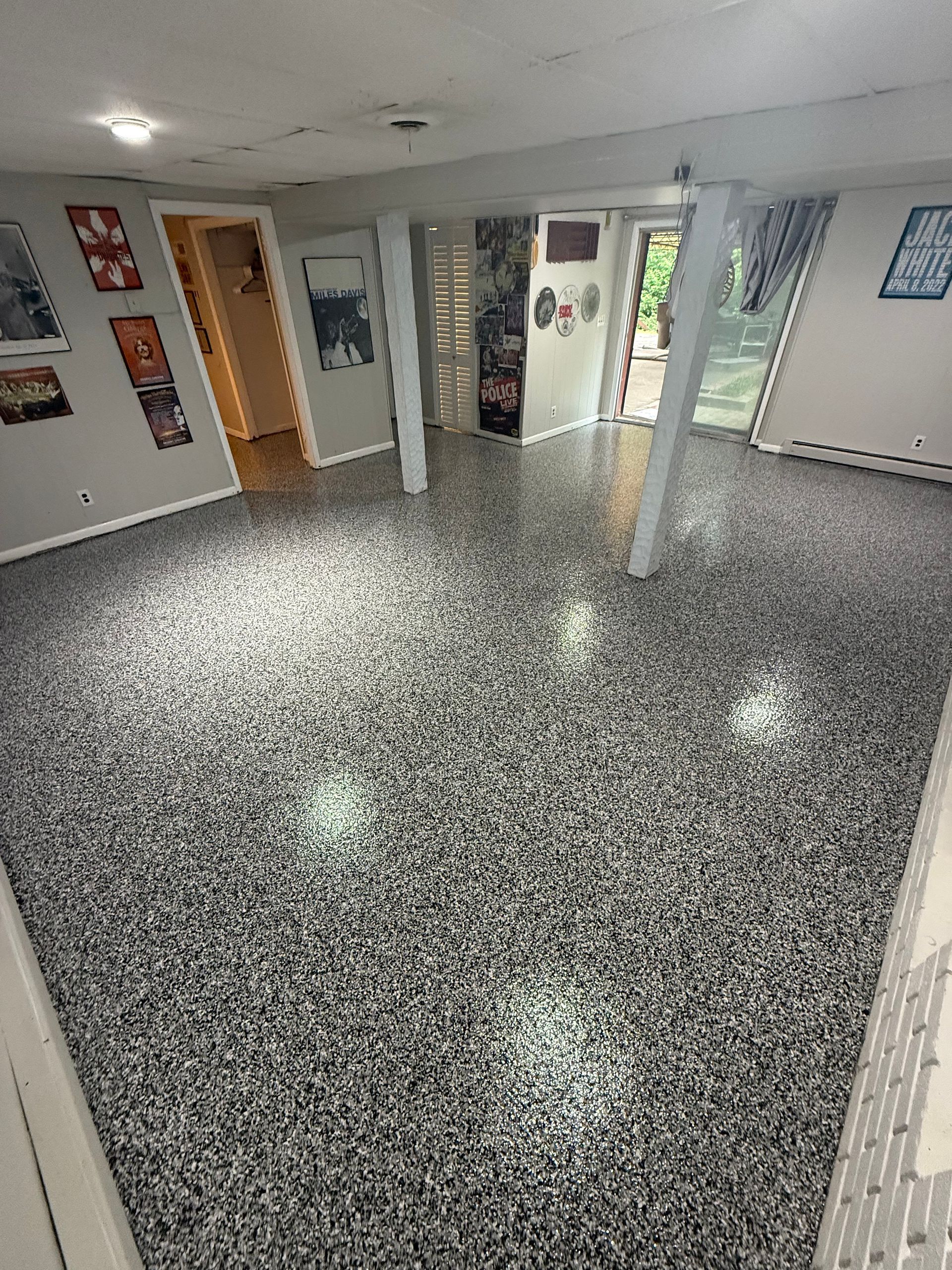 Empty indoor room with glossy speckled floor, white walls, windows, and a central support column