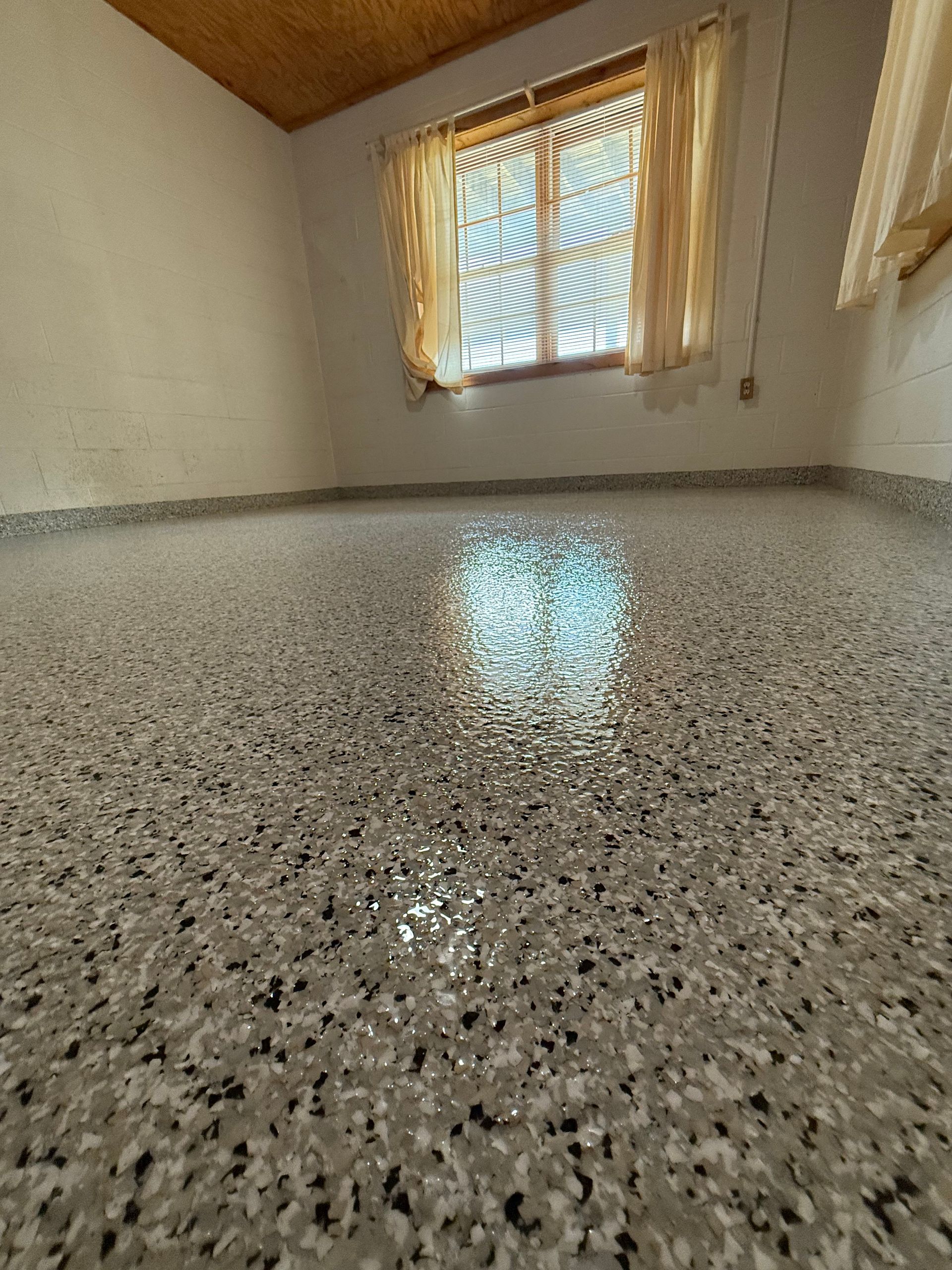 Empty room with glossy speckled floor and a sunlit window with sheer curtains