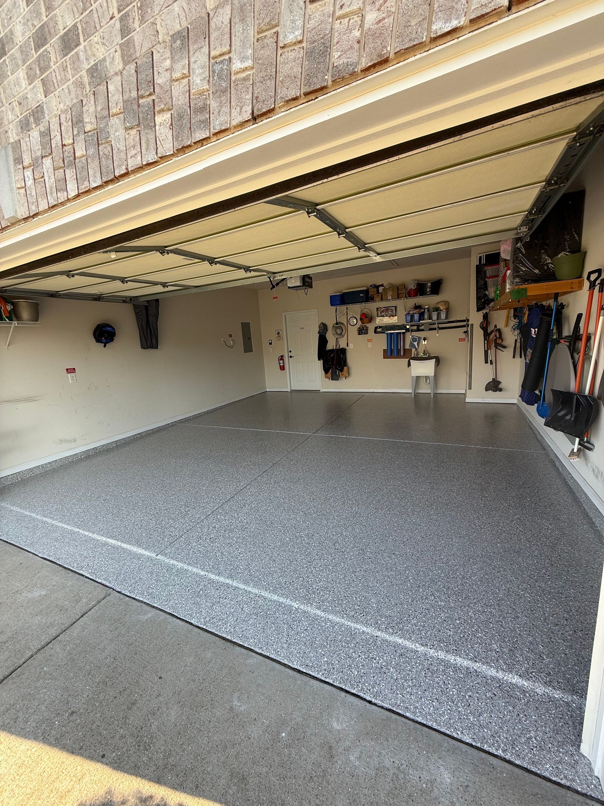 Open garage with a freshly coated gray speckled floor and tools hanging on the walls