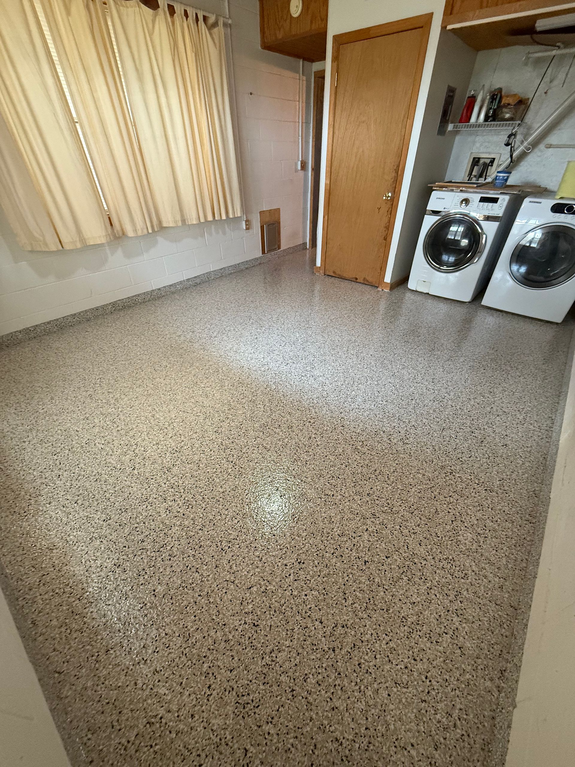 Empty laundry room with speckled tile floor, curtained window, door, and washer and dryer on the right.
