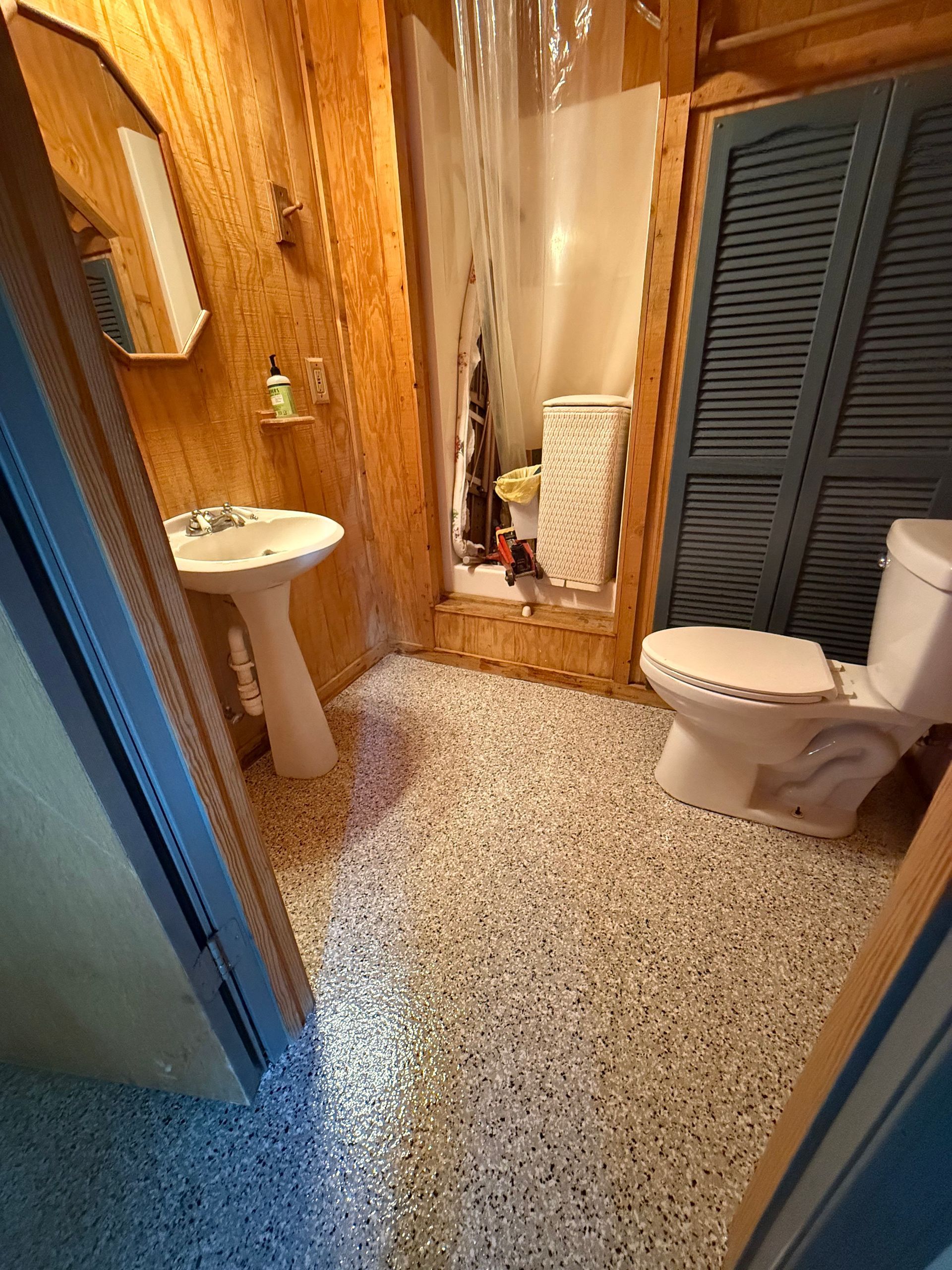 Narrow bathroom with a sink, toilet, shower curtain, and wood-paneled walls.
