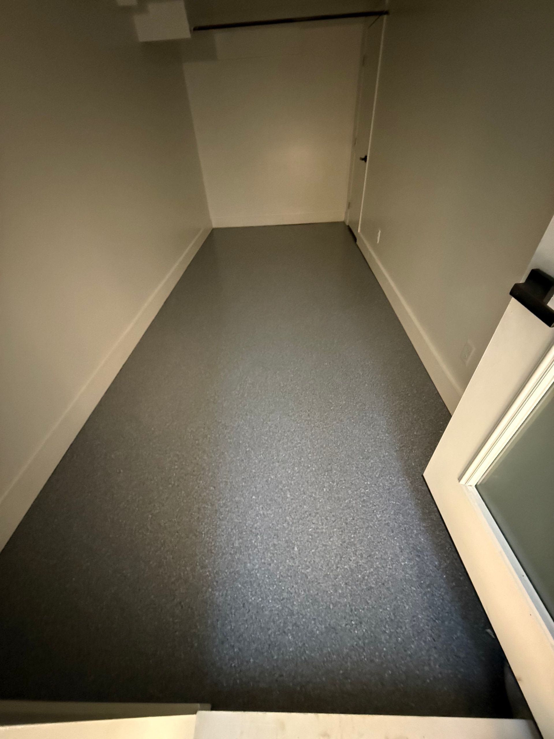 Empty narrow hallway with gray flooring and beige walls, ending at a closed door.