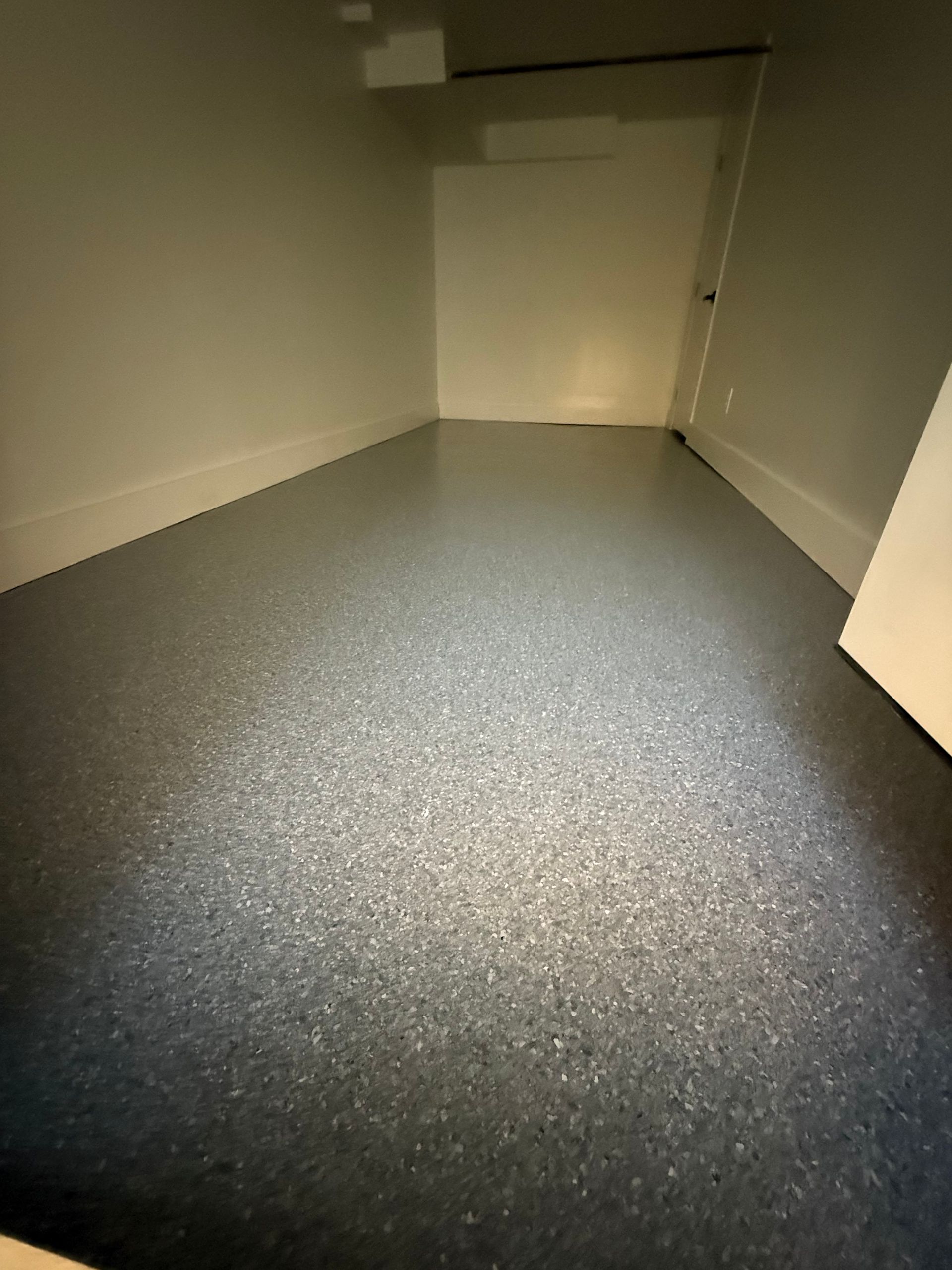 Empty gray-floored storage room with beige walls and a door at the back