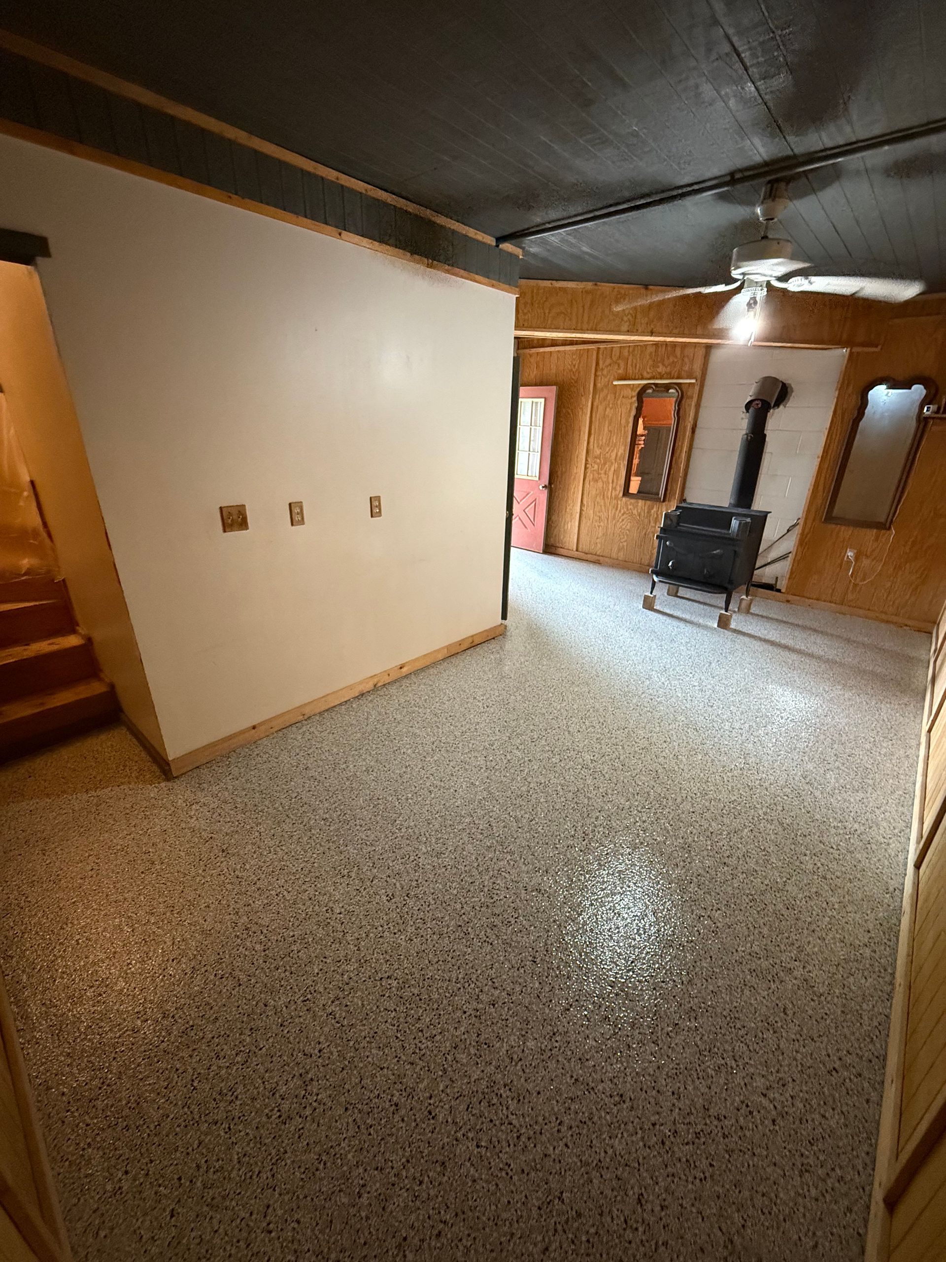 Empty tiled living room with white walls, wood stairs, and a black stove near a window.