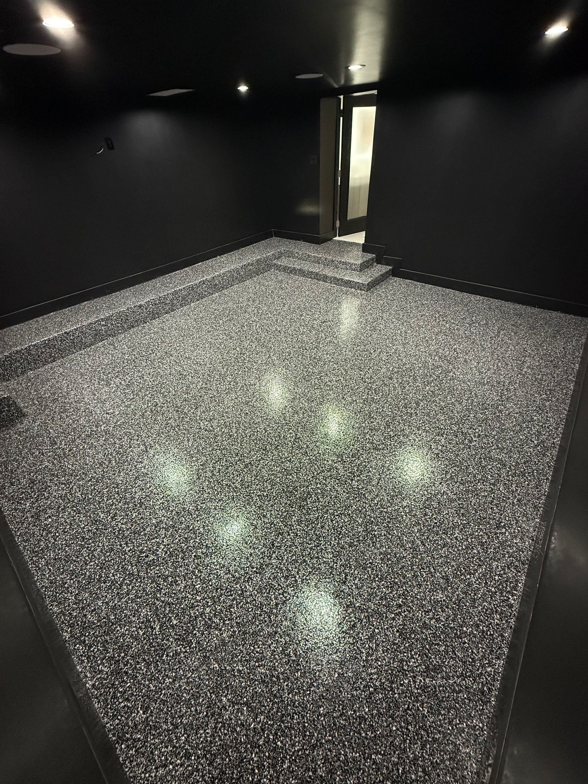 Dark room with a glittering silver floor and black walls, lit by small ceiling spotlights.