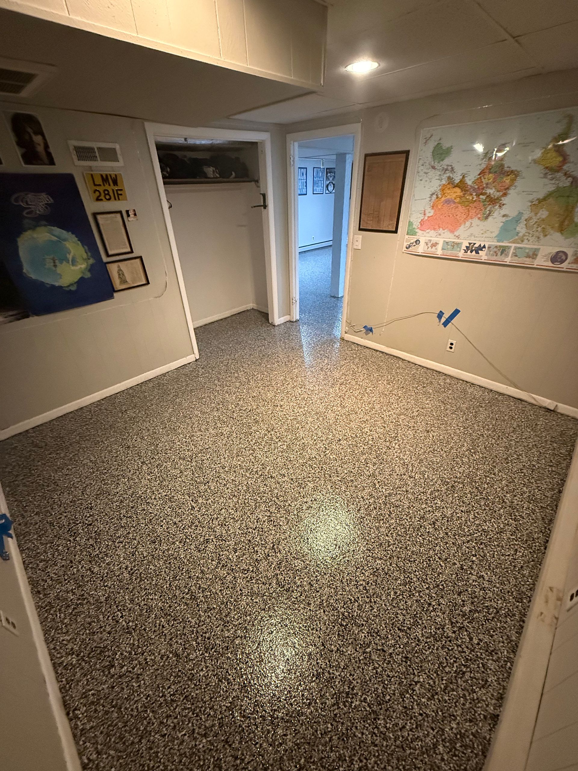 Empty speckled room with white walls, posters, and an open doorway to a hallway.