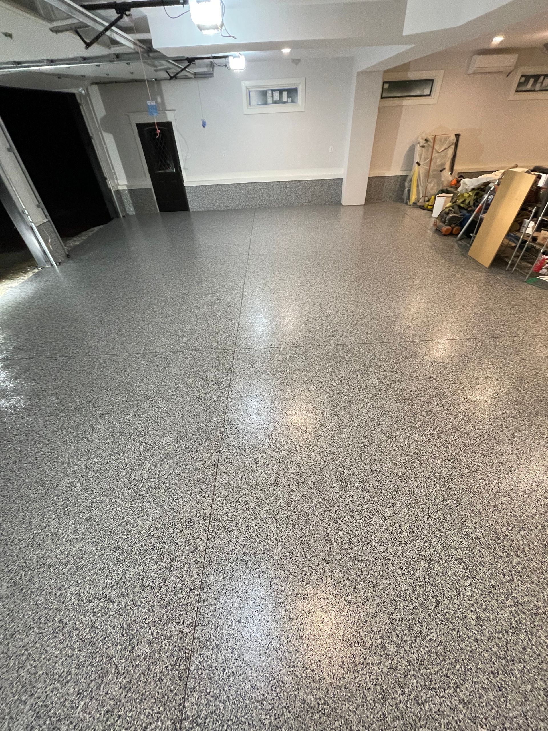 Empty indoor garage with speckled gray floor, white walls, and storage items along the right side.