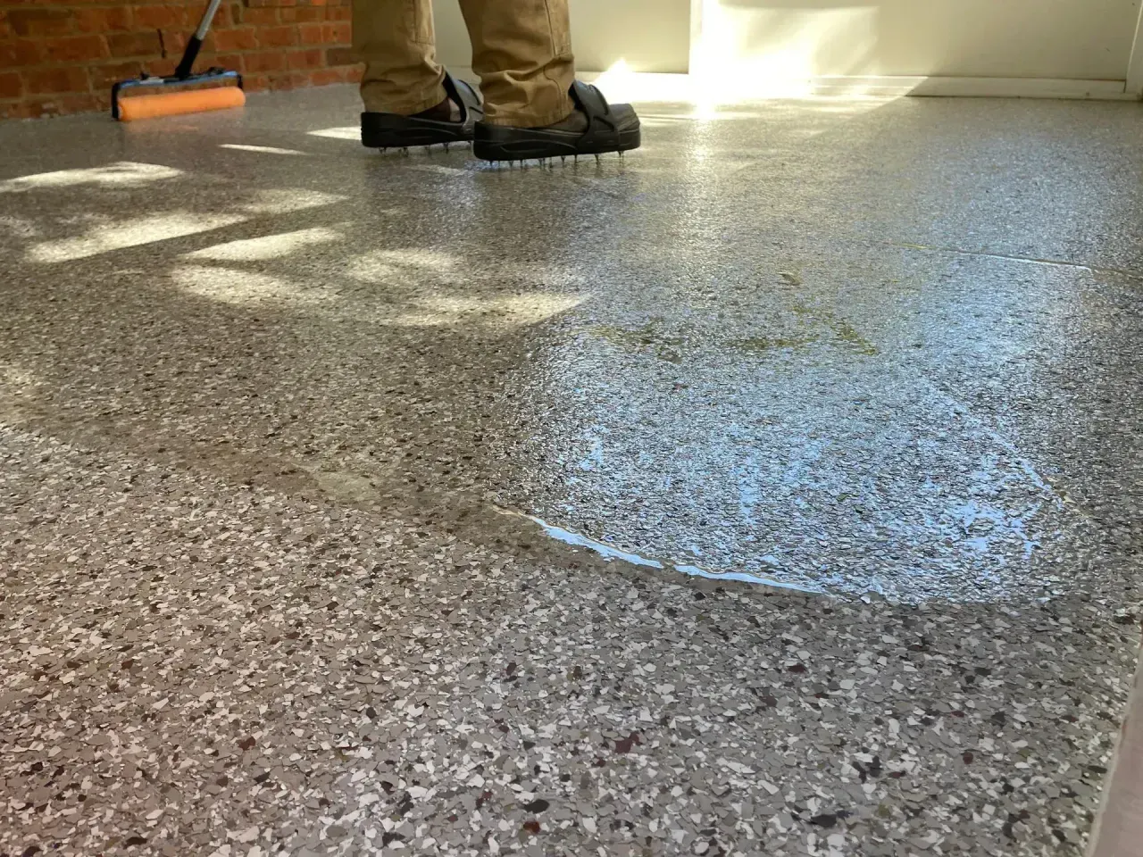Person polishing a speckled floor with a buffer in a sunlit room