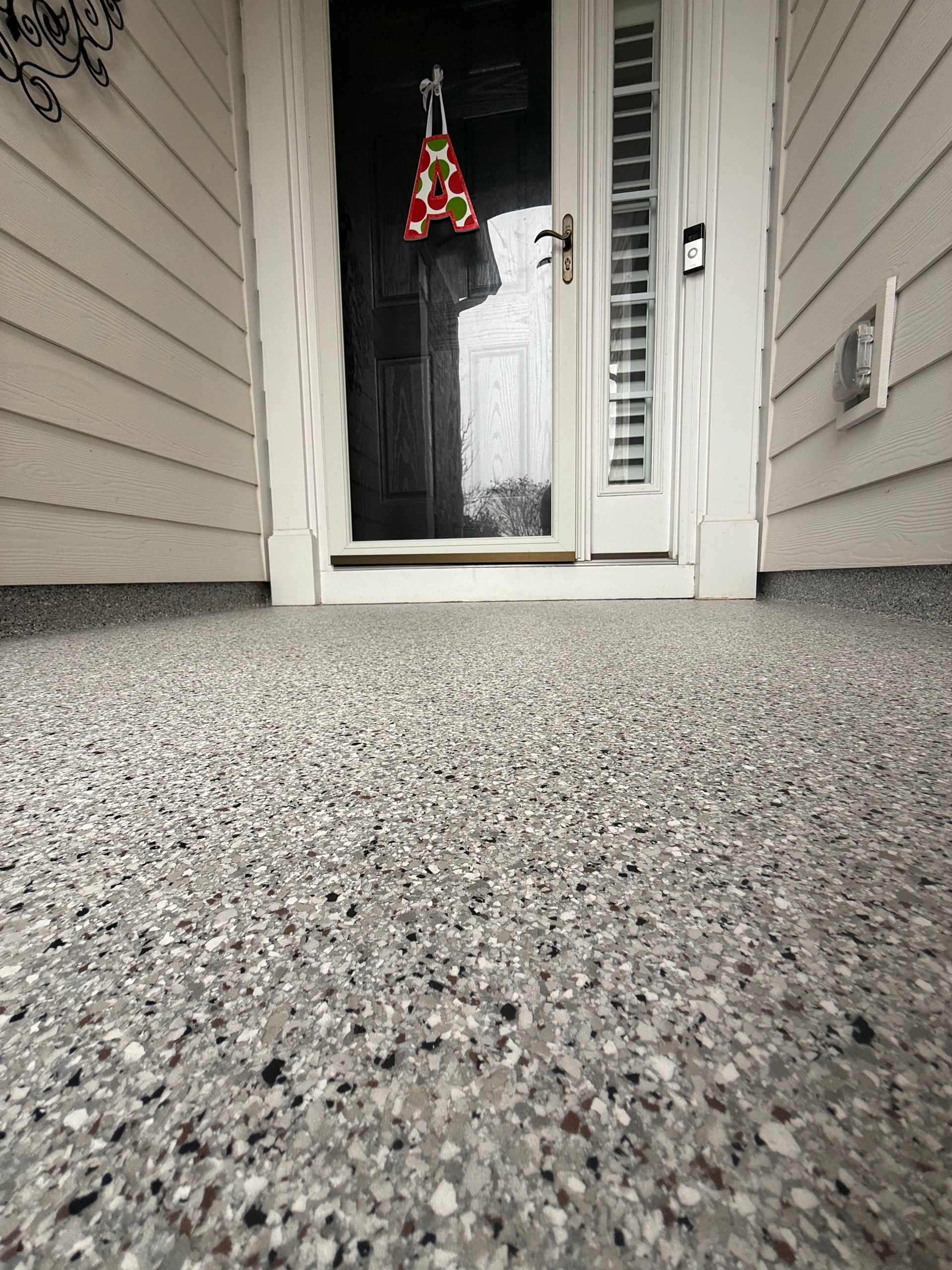 Low-angle view of a front porch with gray pebbled flooring, a glass door, and hanging holiday decoration