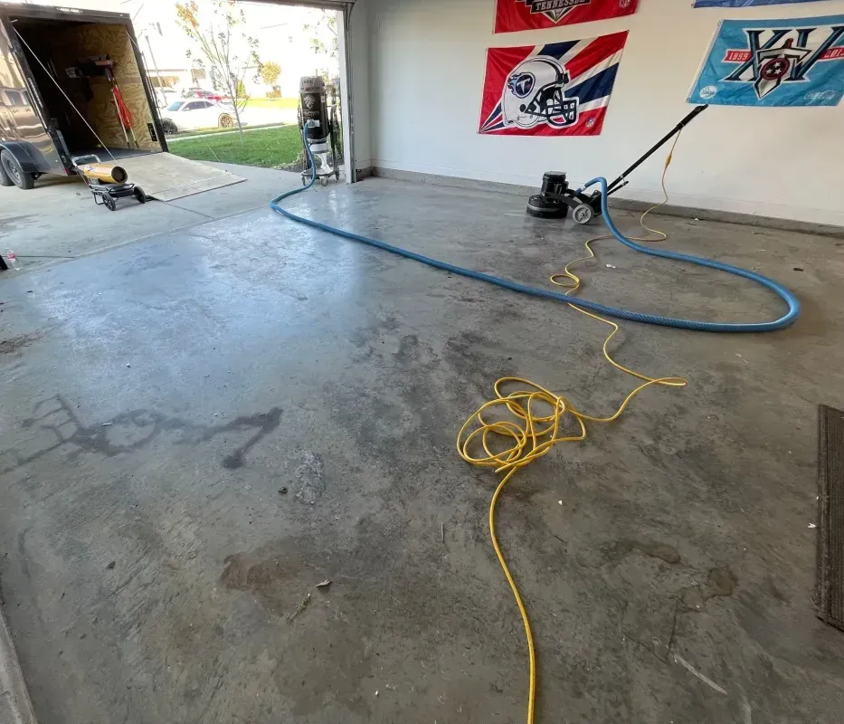 Garage floor with blue hose and yellow cord, car on a lift, and wall banners in the background