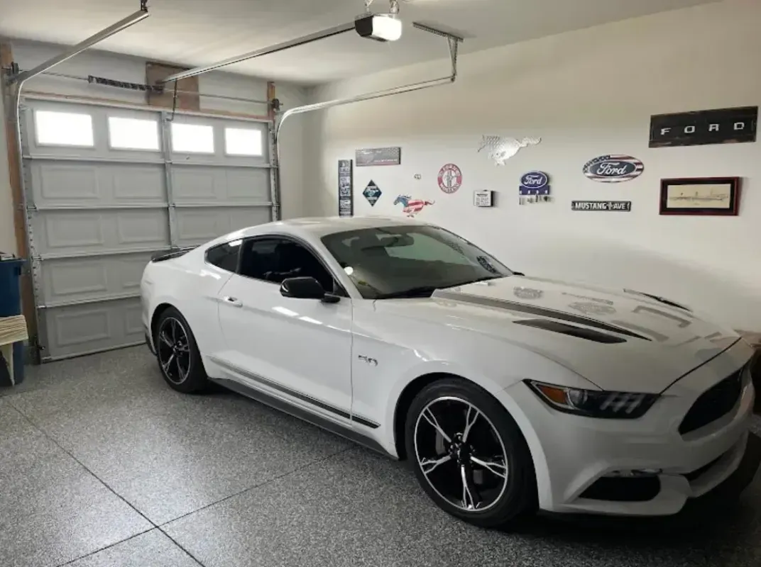 White sports coupe parked in a bright garage with garage door and wall decor.